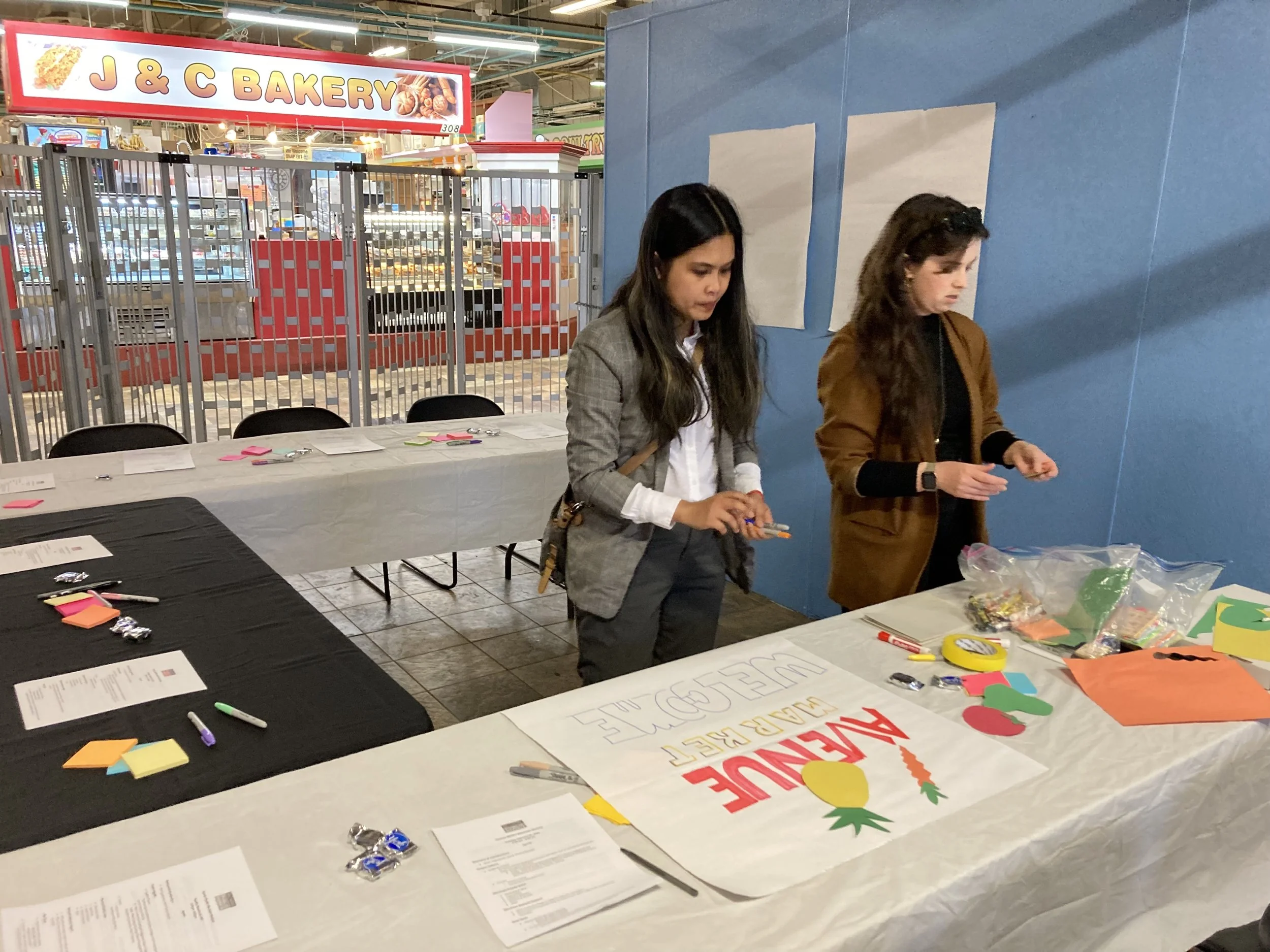 Two people working at a table with colorful paper cutouts and markers, in preparation for a merchant meeting for the redevelopment of Avenue Market in Baltimore.