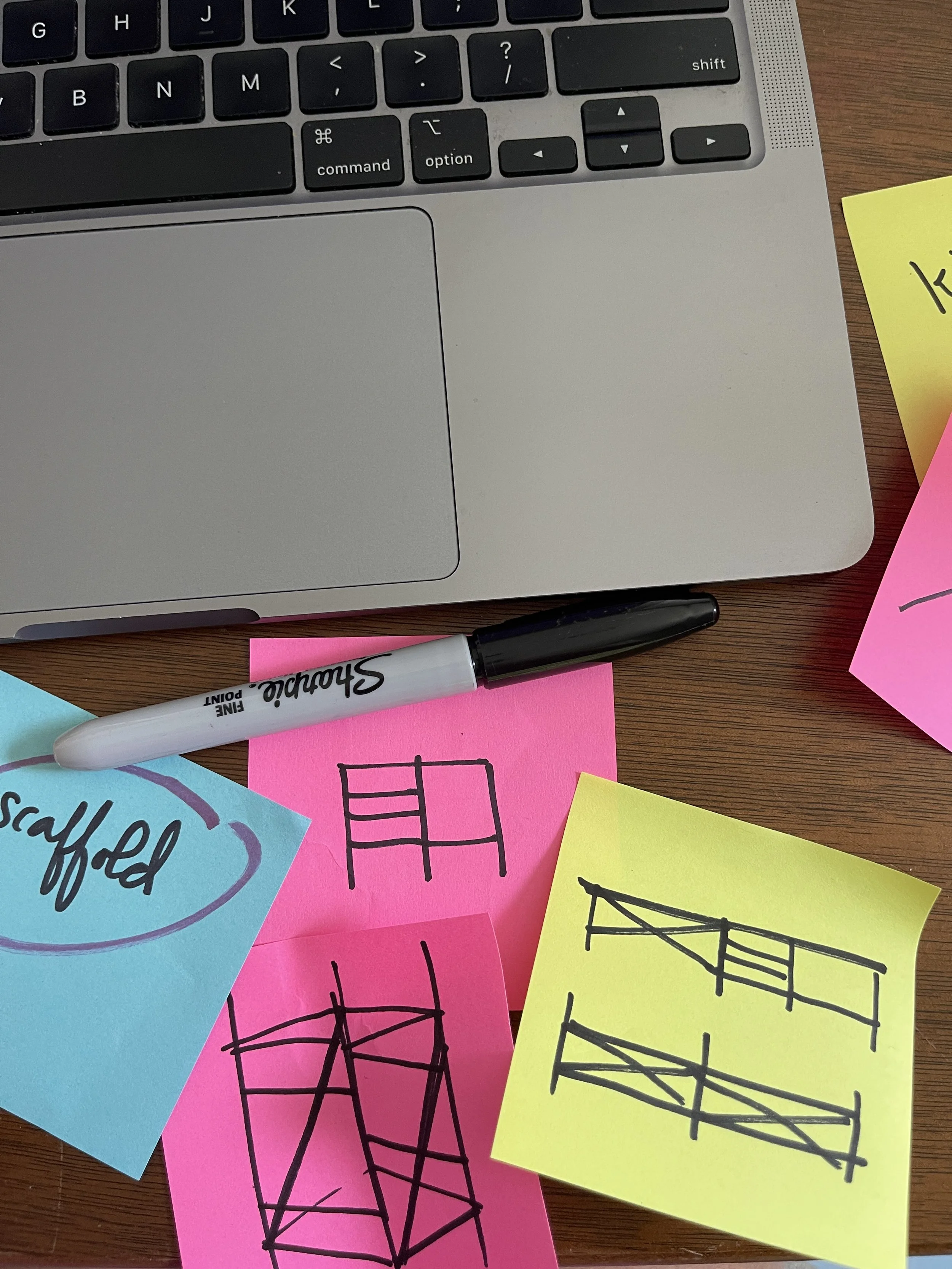 A workspace with a laptop keyboard, colorful sticky notes with hand-drawn sketches of structures, and a Sharpie marker.