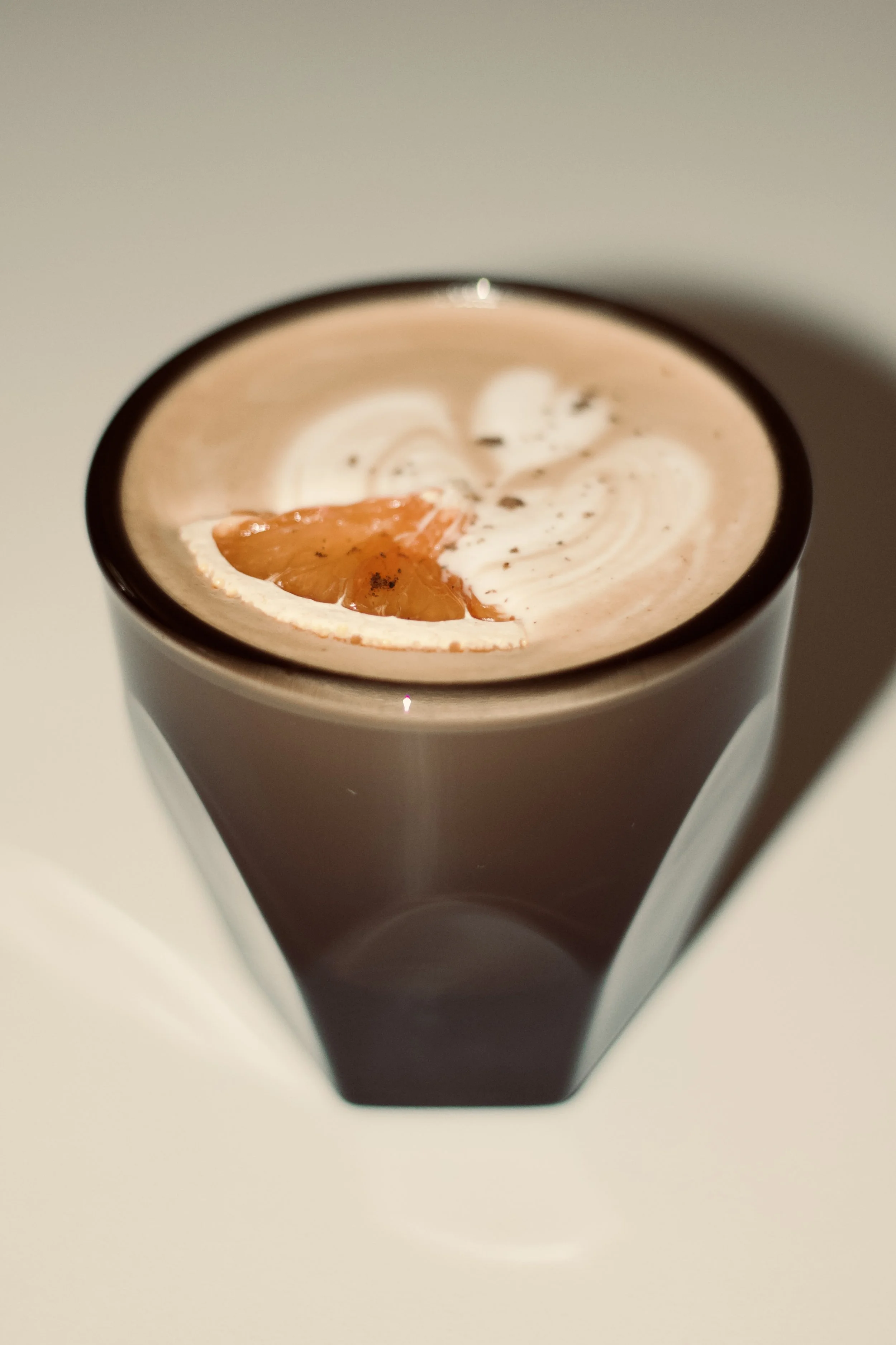 A tall glass of chocolate drink topped with whipped cream, garnished with a citrus slice and chocolate shavings.