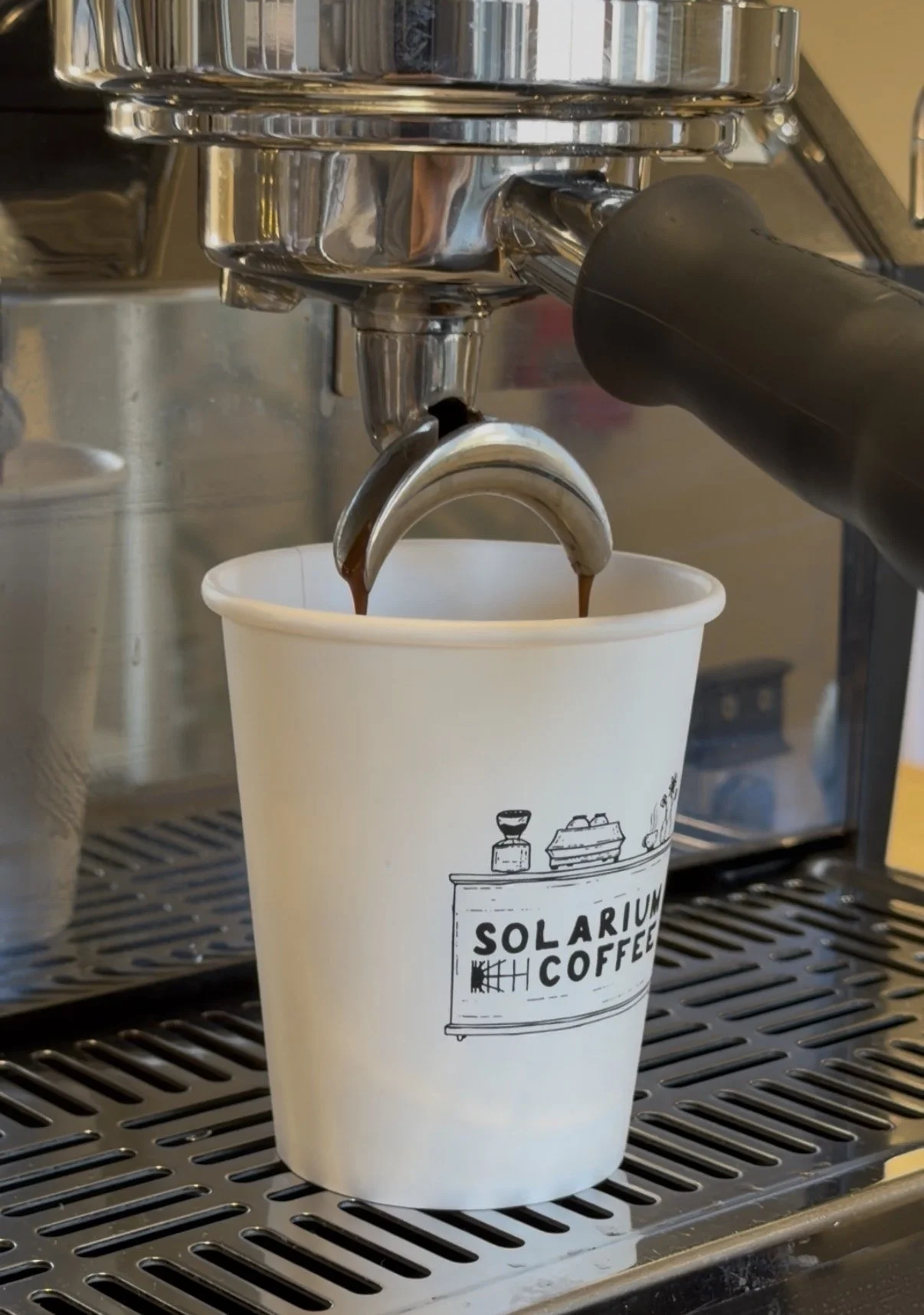 Espresso machine pouring coffee into a paper cup with 'Solarium Coffee' logo.