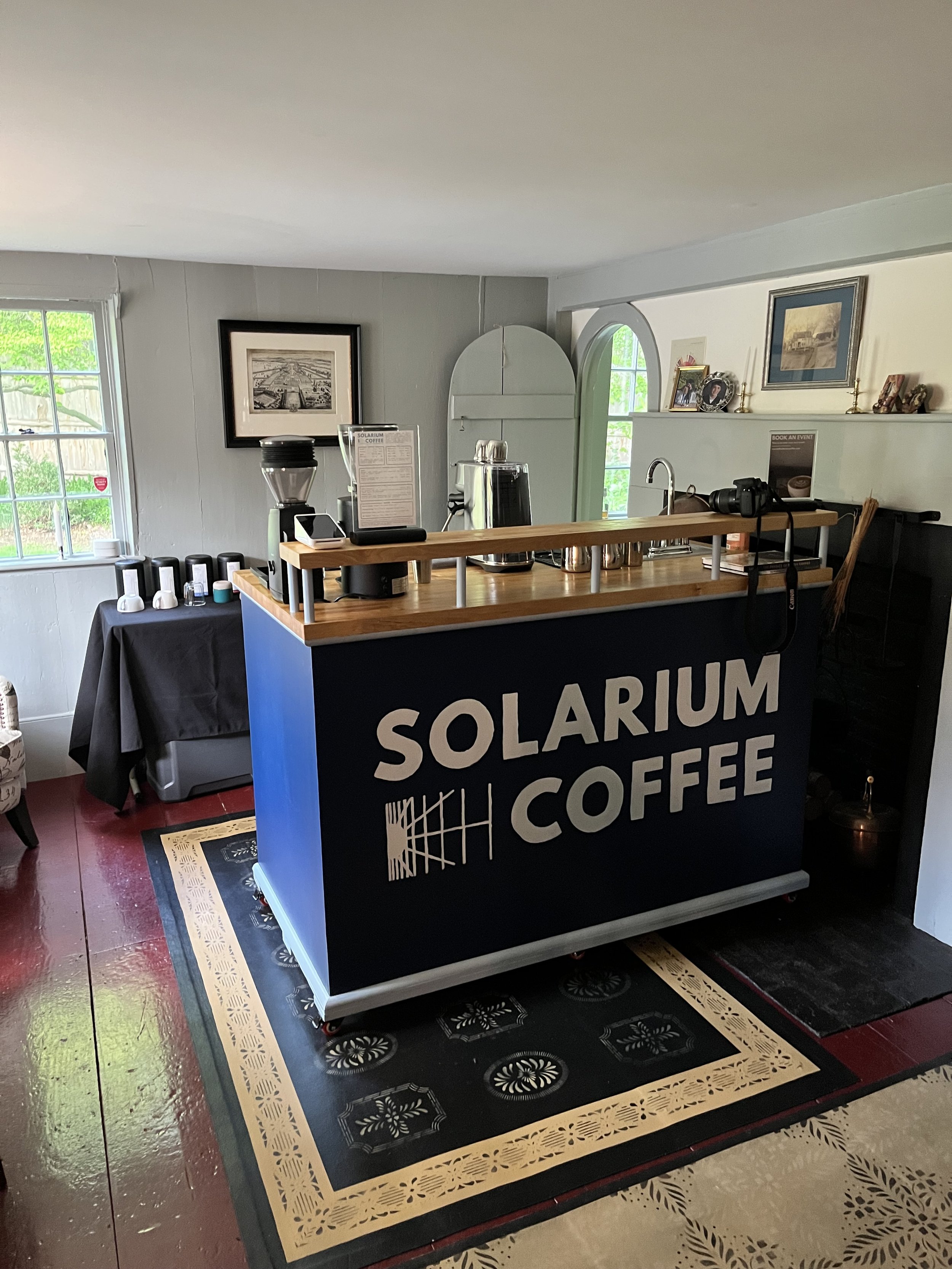 Interior of a coffee shop with a counter labeled 'Solarium Coffee', coffee brewing equipment, cups, and decorative framed pictures on the walls.