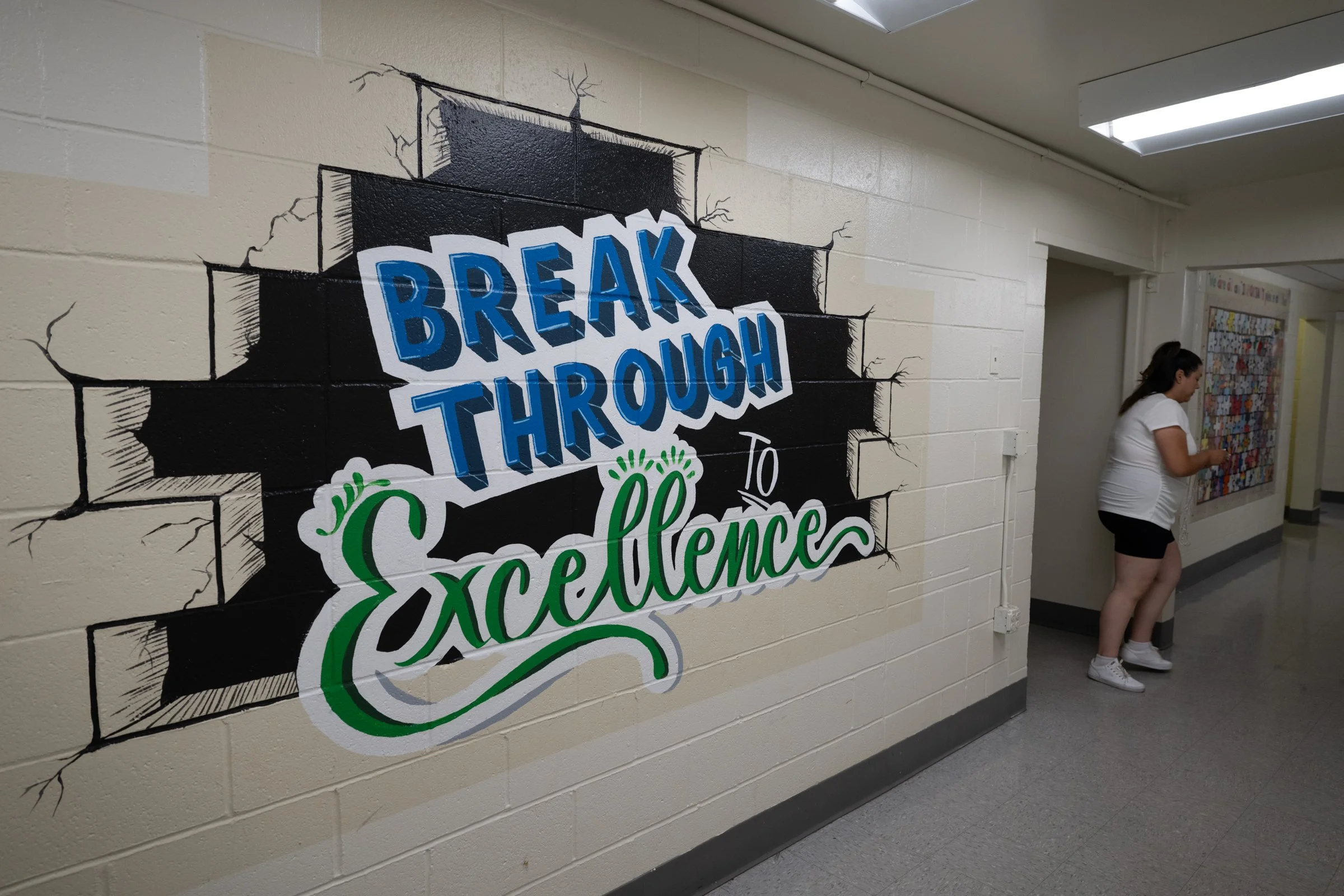 Wall mural with a painted brick wall background stating 'Break Through to Excellence' in bold blue and green letters, with illustrations of crack marks around the words.