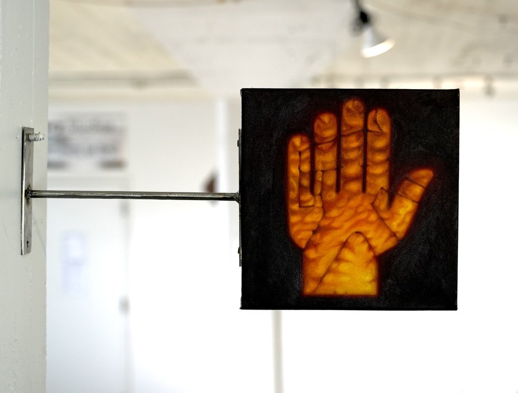 A sculptural painting of an orange hand affixed to the wall with a steel mount.