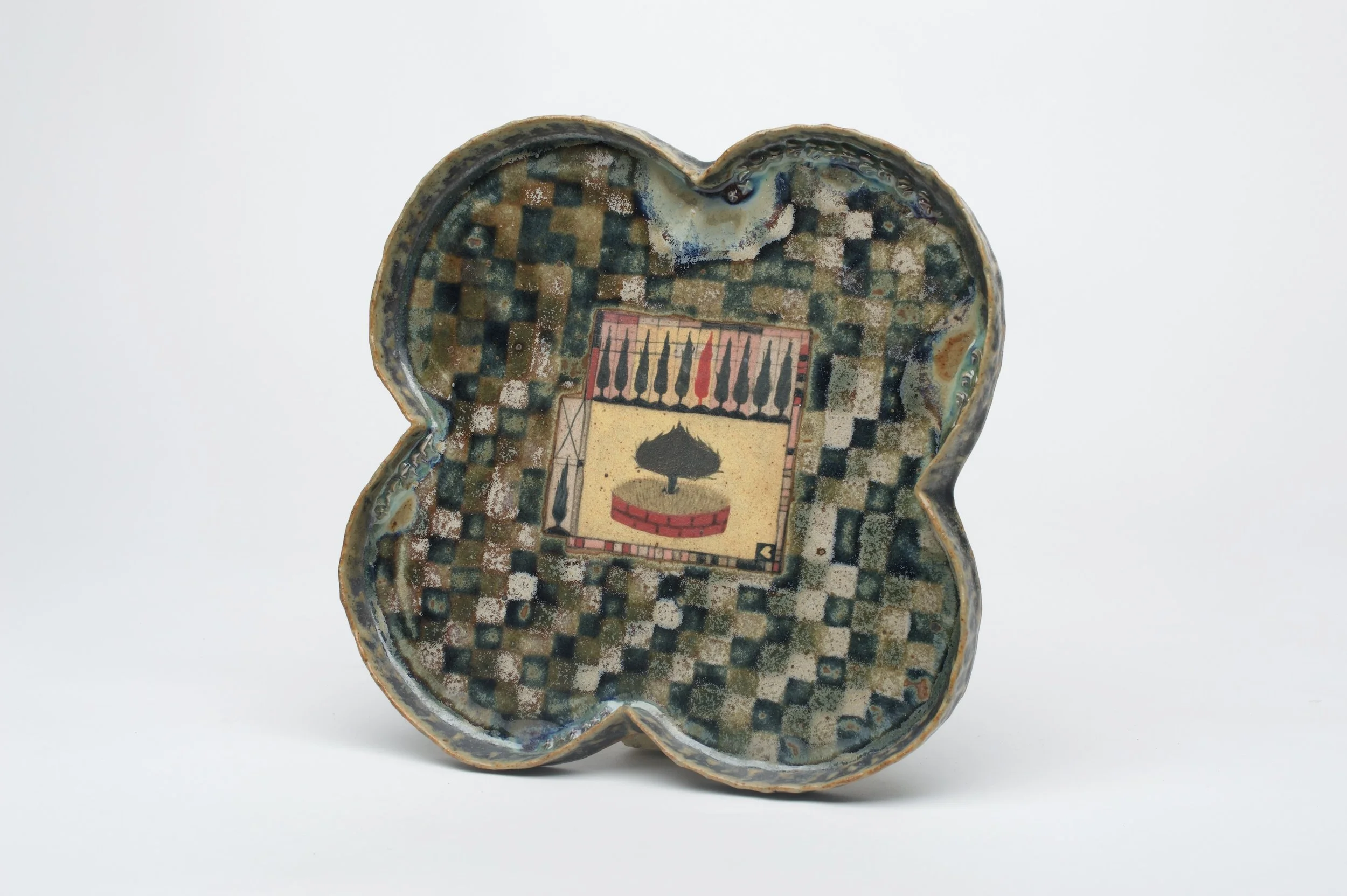 A quatrefoil plate with a multi tonal green checker pattern around a central image of cypress trees.