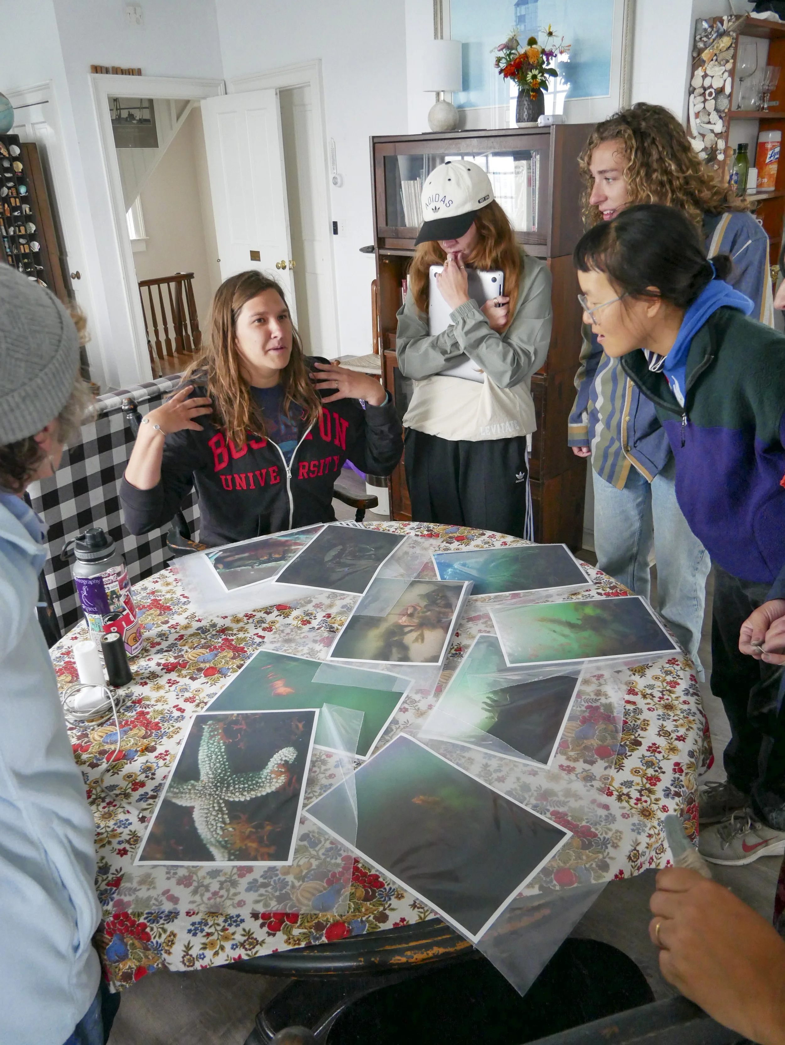 A group of people gathered around a table looking at and discussing photographs.