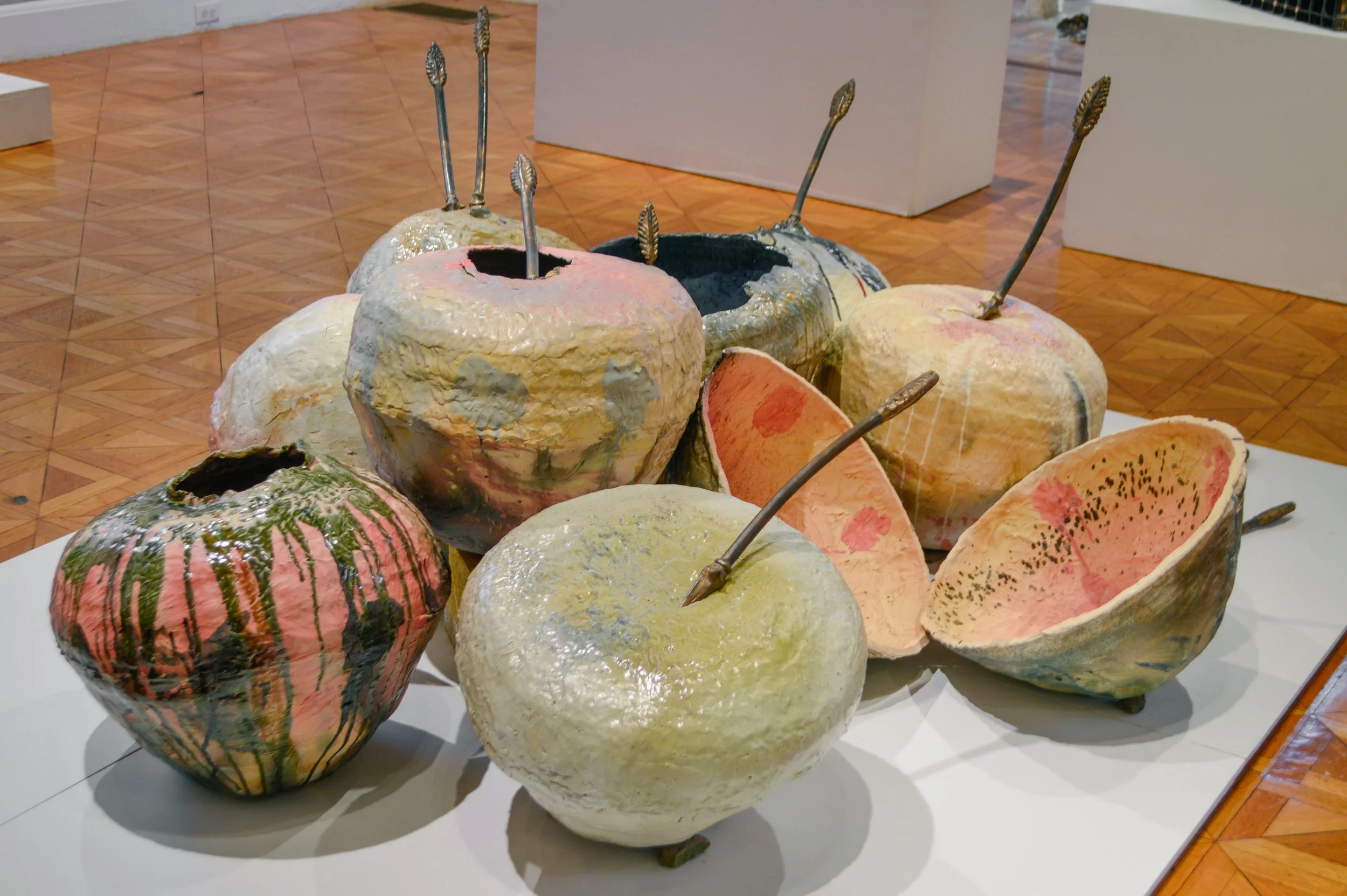 A collection of large-scale ceramic sculptures that resemble cherries in a pile on a gallery floor.