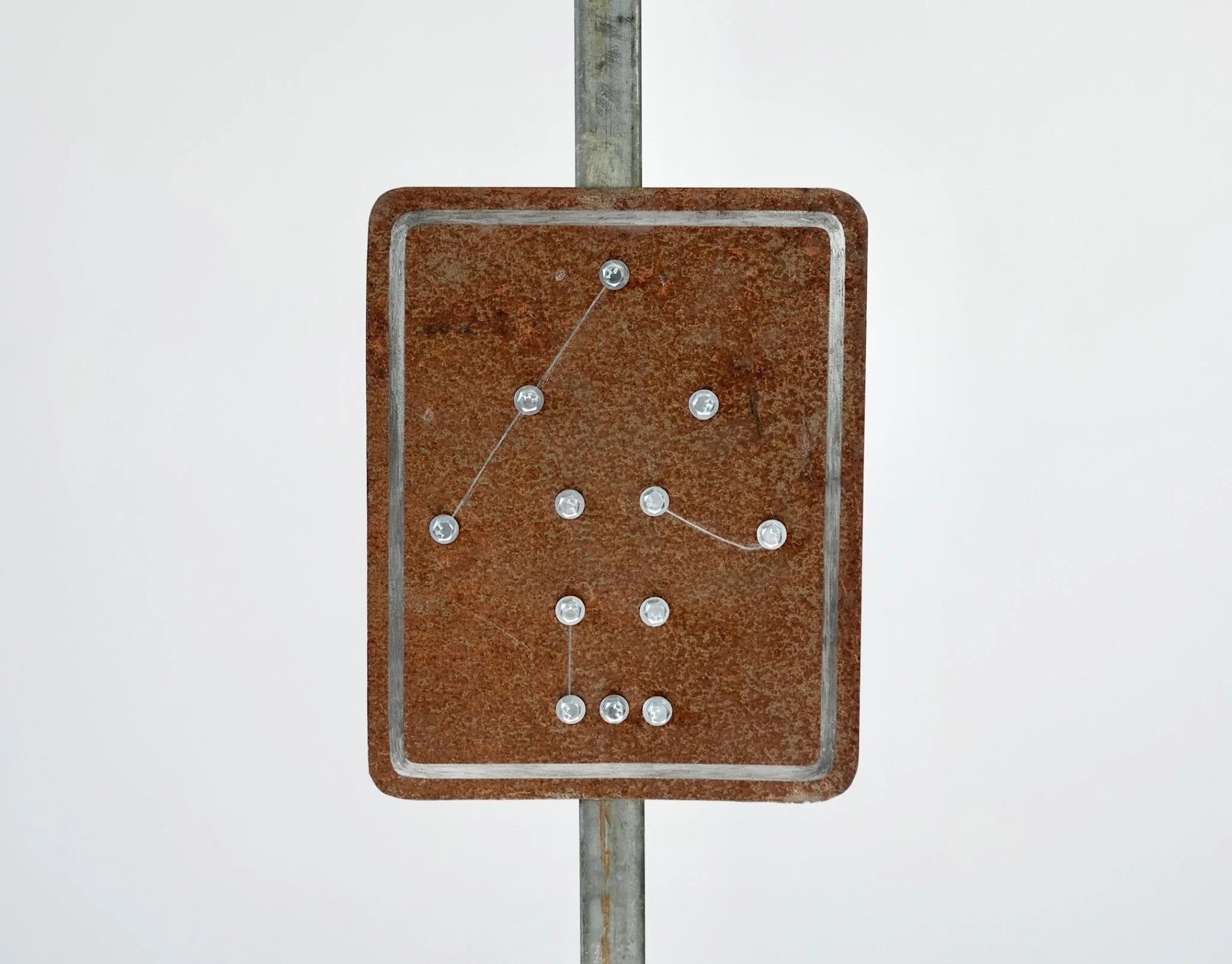 A patinated steel sculpture in the shape of a rod sign with dots.