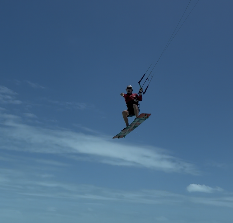 Person kiteboarding mid-air against a cloudy blue sky.