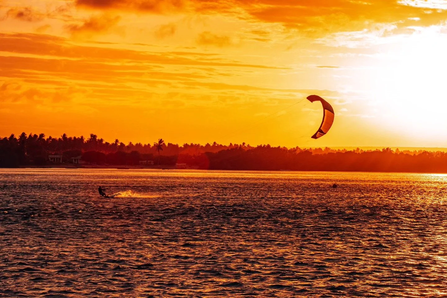 Sunset over water with a kite surfer in the water and a kite flying in the sky.