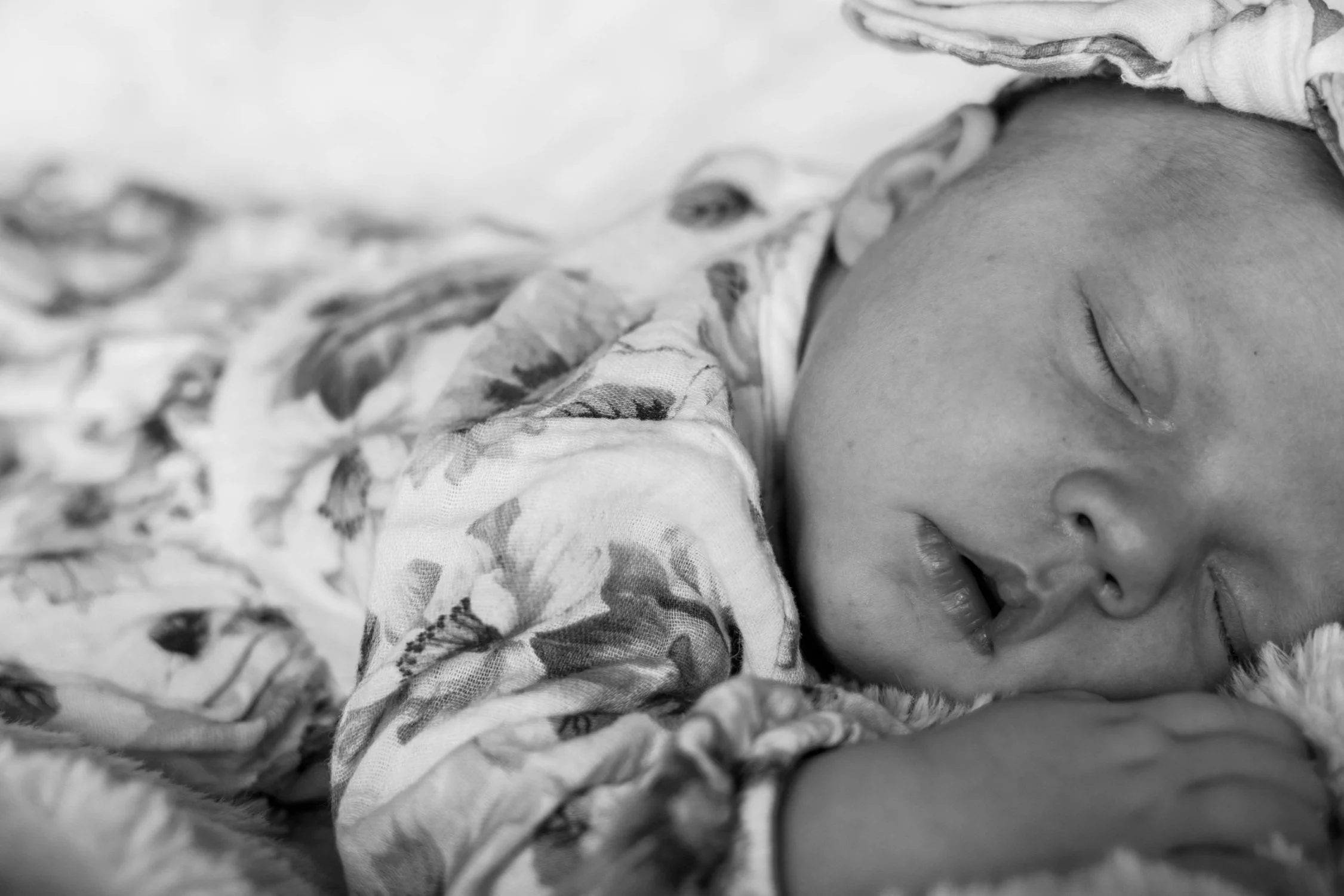 Close-up of a sleeping newborn baby with closed eyes, lying on a soft surface, wrapped in a patterned fabric.