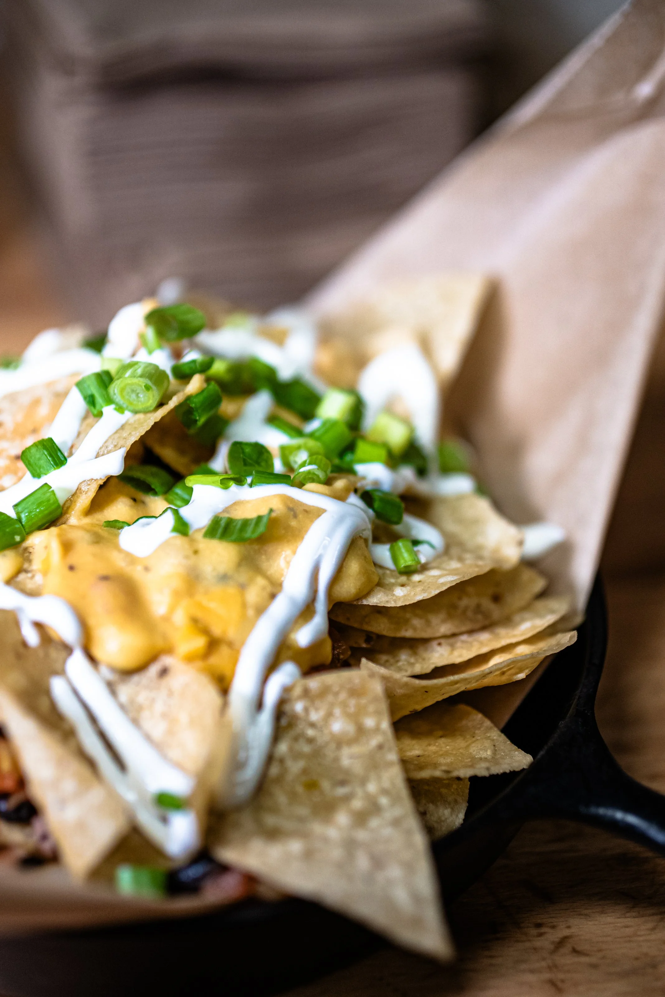 Close-up of nachos topped with melted cheese, sour cream, and chopped green onions on a black plate.
