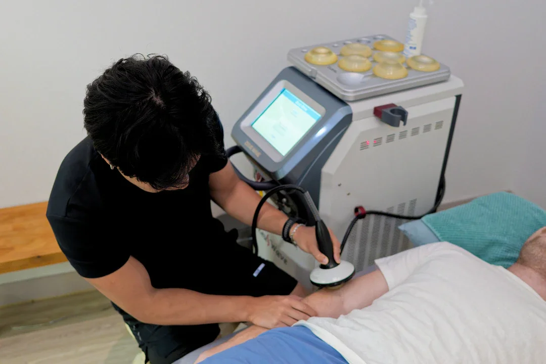 A healthcare professional using a medical device on a patient's arm in a clinical setting.