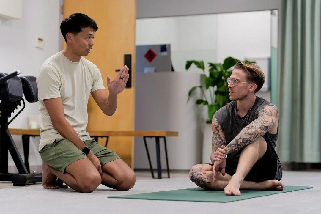 A male physiotherapist explaining the spinal movement to a client on a yoga mat