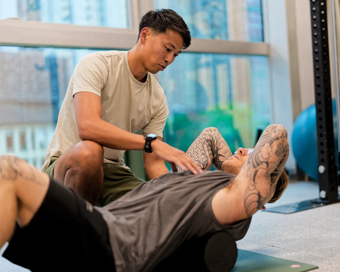 A personal trainer helps a man with tattoos during an abdominal workout at a gym.