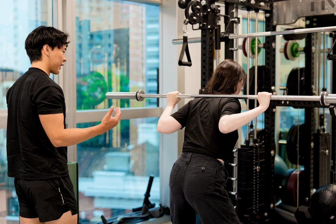 Women lifting a barbell with a trainer coaching in a gym.