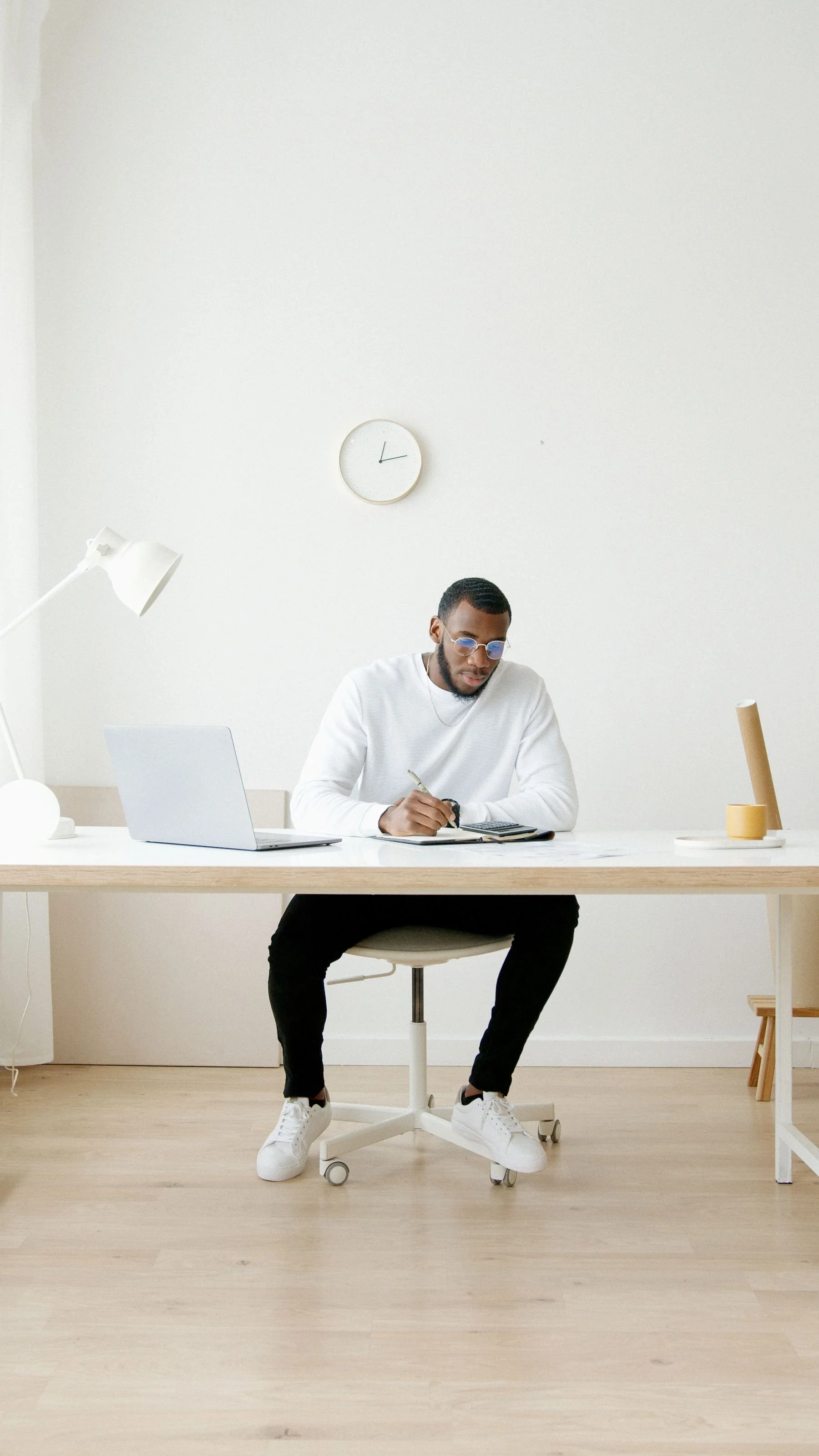 A professional writing in a notebook beside a laptop at a desk.