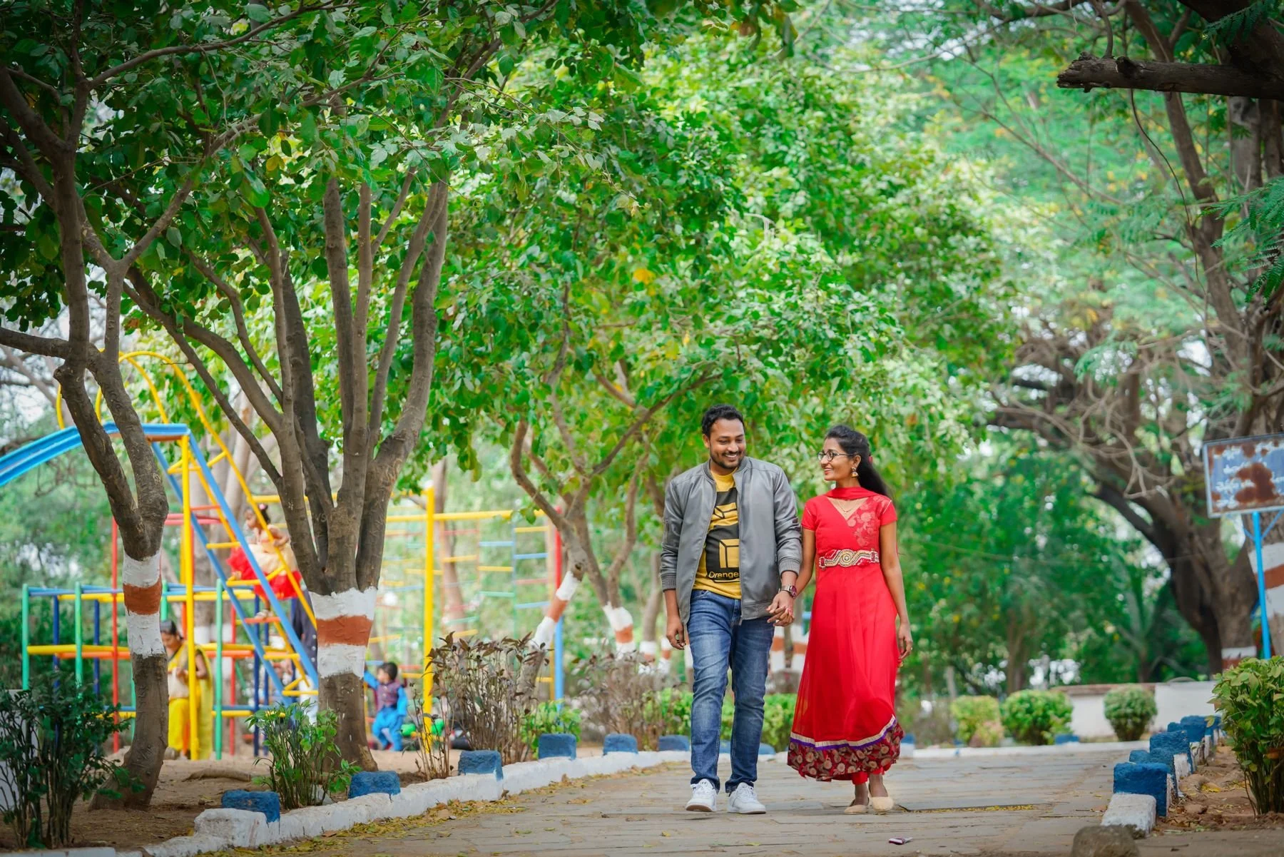 Two people holding hands while walking along a path in a green park.