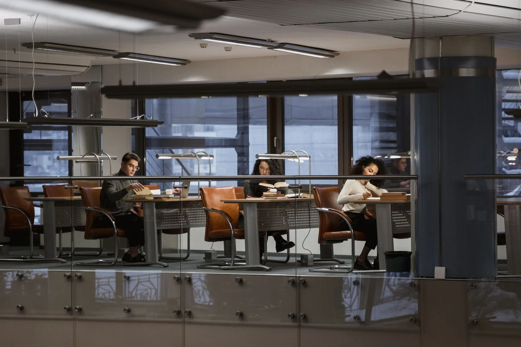 Three adults studying with books at separate tables in a modern library.