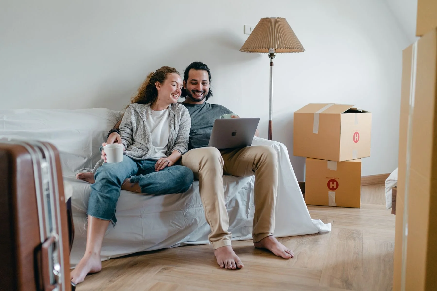 Two adults looking at a laptop on a sofa with moving boxes nearby.
