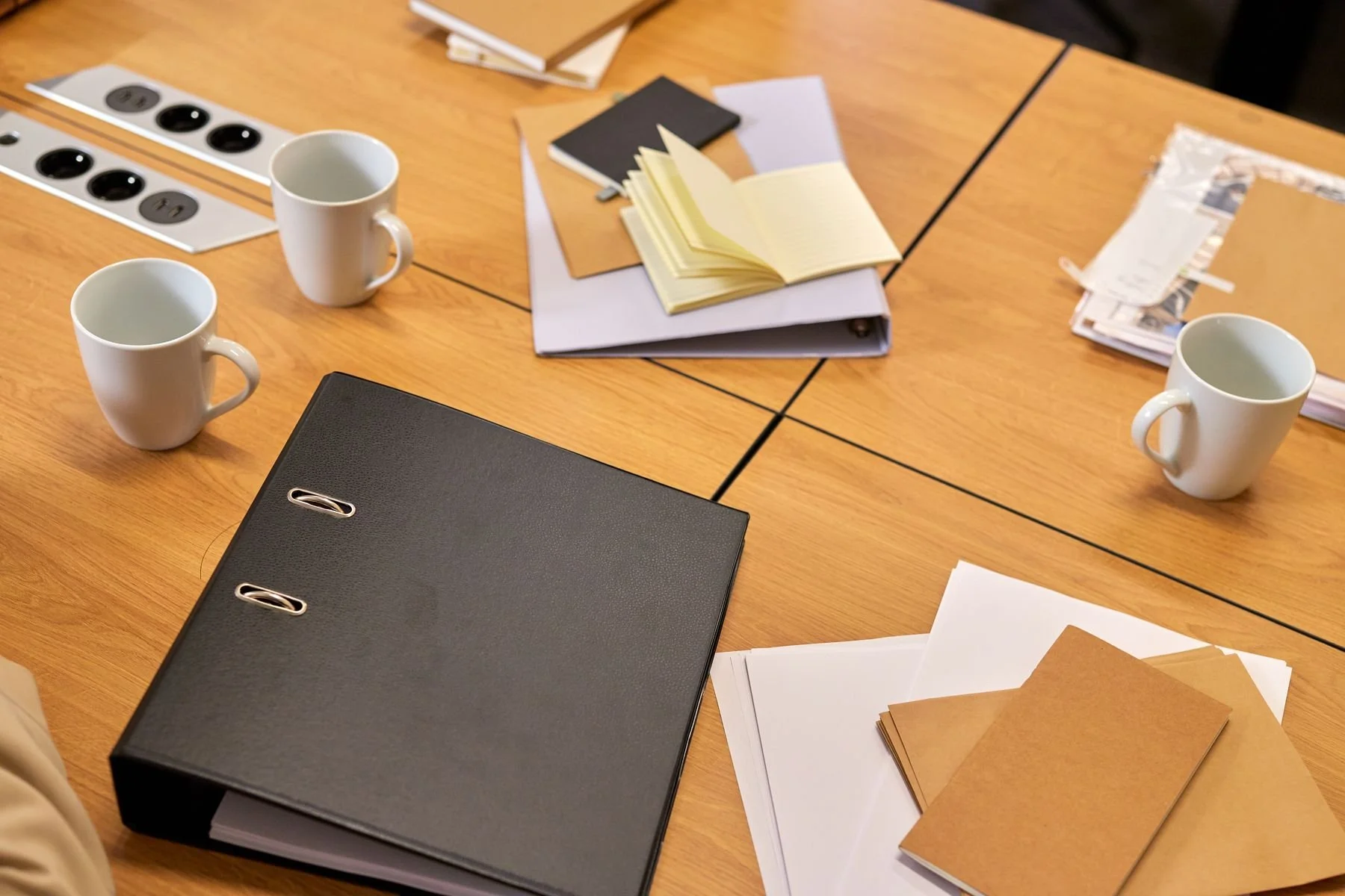 Binders, loose papers, notebooks and coffee mugs arranged on a large desk.