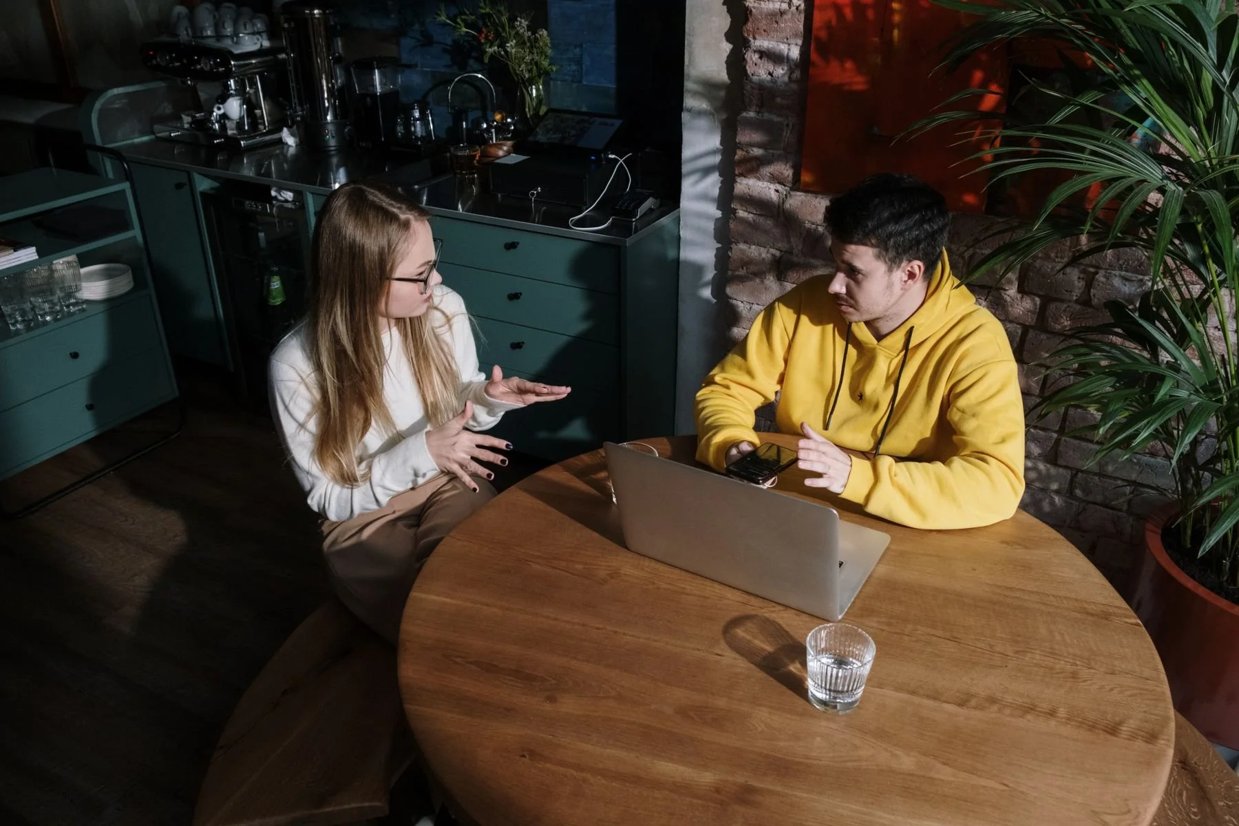 Two adults discussing information across a laptop at a café table.