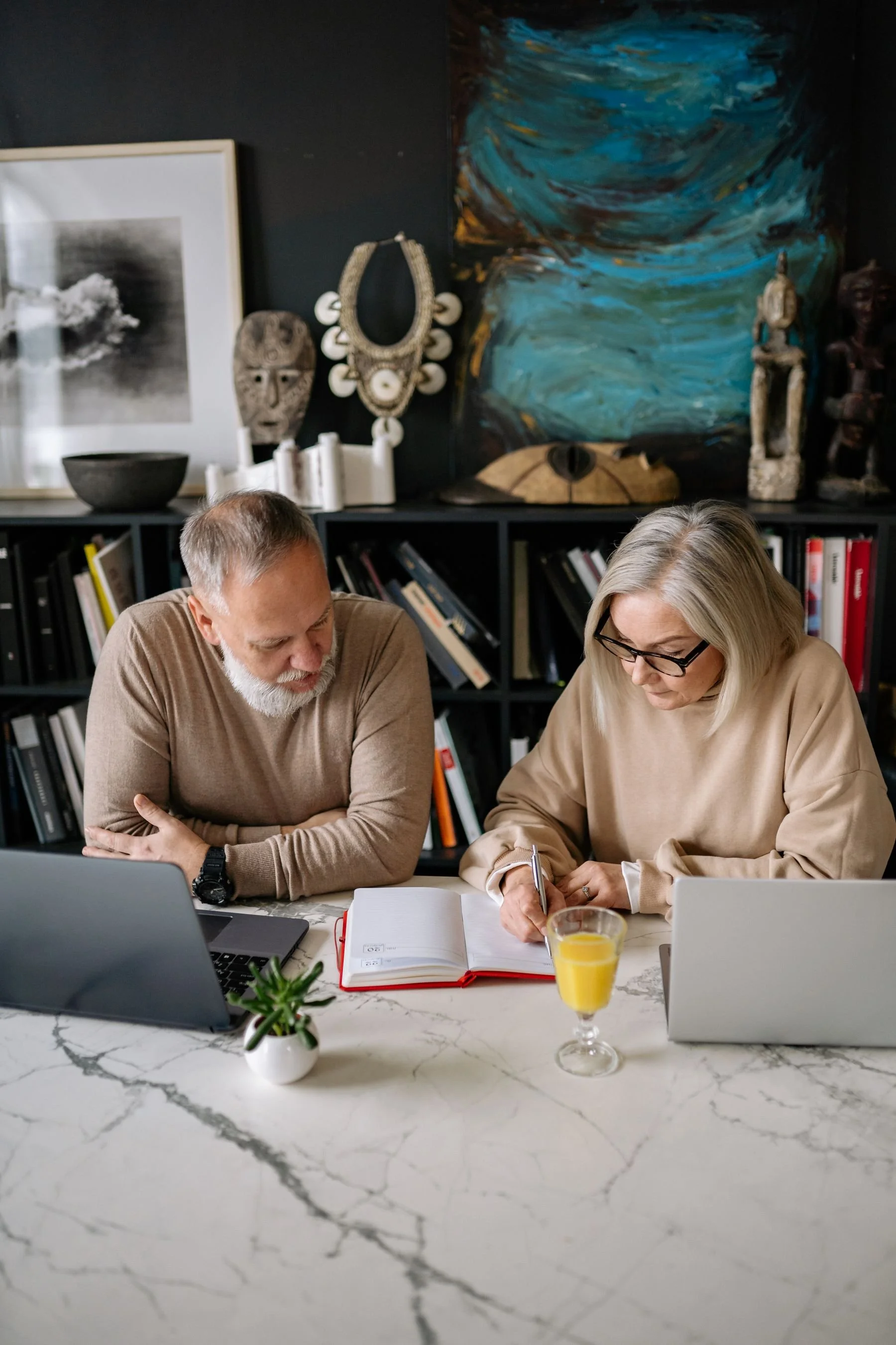 An older couple working at a table with laptops and an open planner.