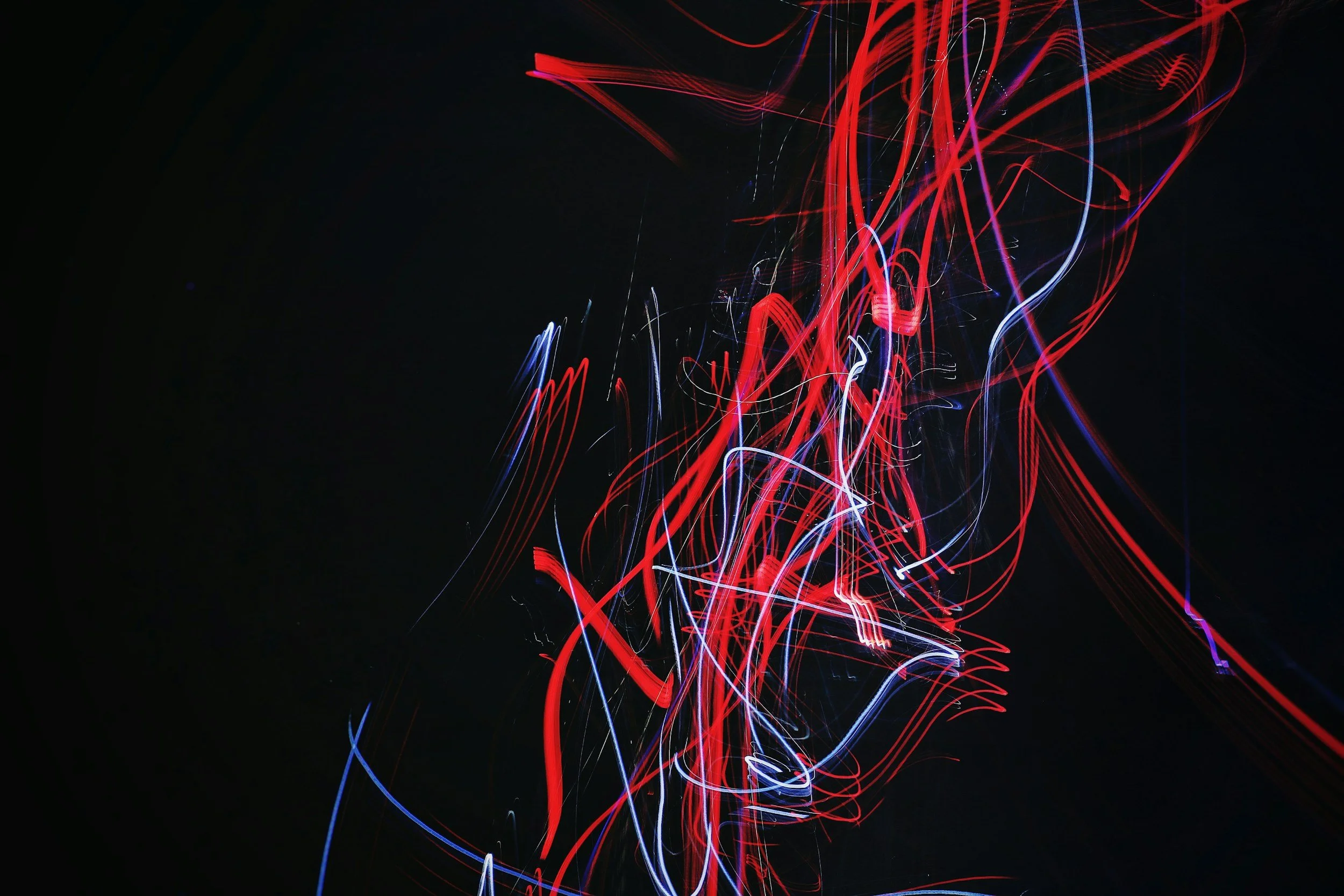 Abstract light trails in red, white, and blue against a black background.