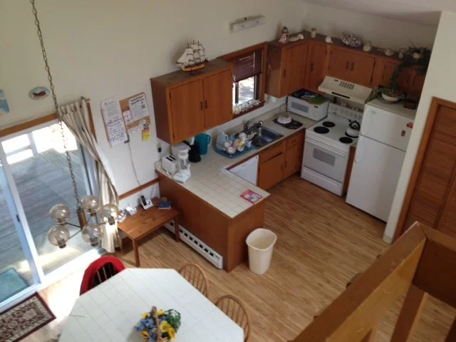 An overhead view of a kitchen and dining area with wooden cabinets, a white stove, refrigerator, microwave, a circular dining table with a floral centerpiece, and a sliding glass door with curtains leading to an outdoor patio.