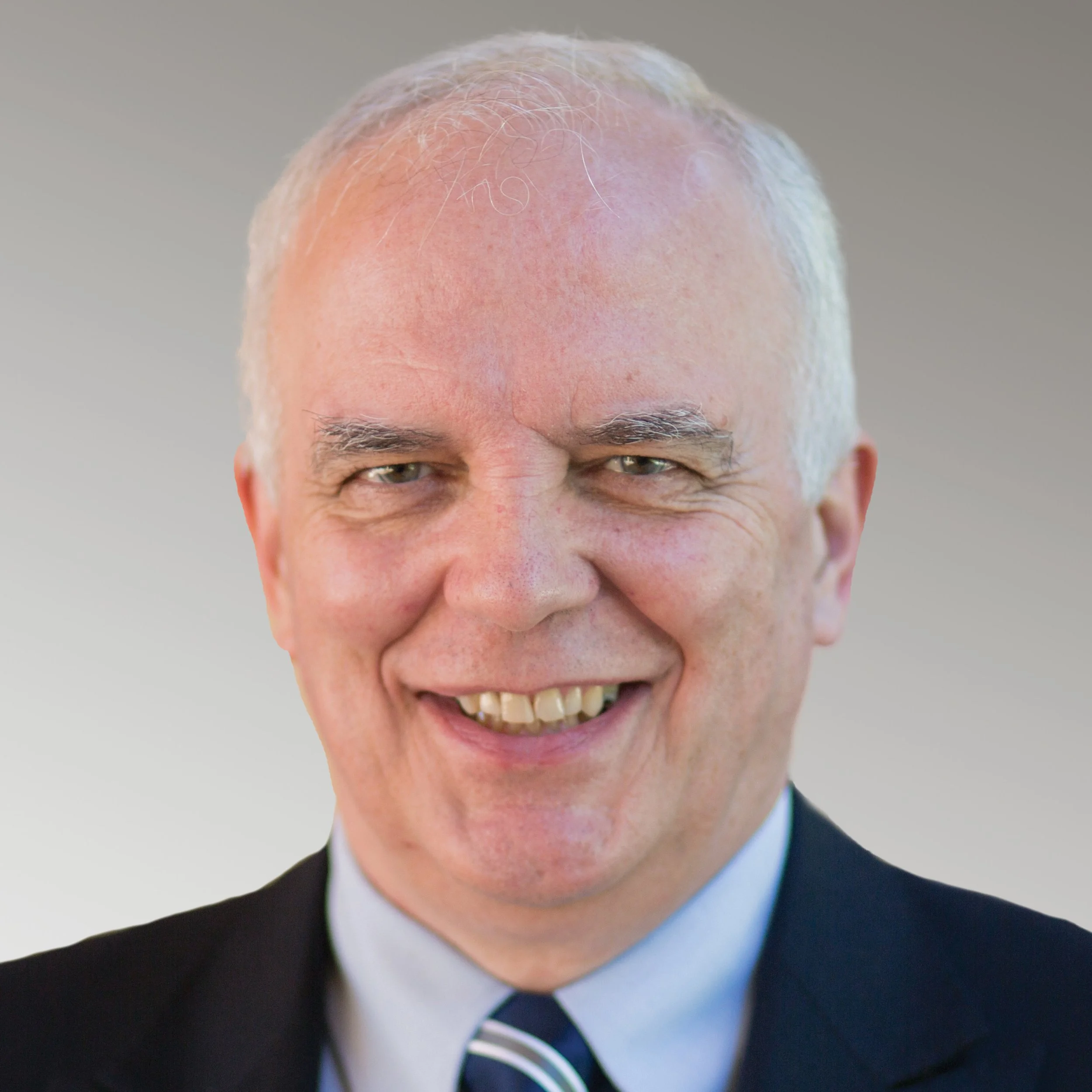 Smiling man with short hair and beard wearing a suit and tie, neutral background.