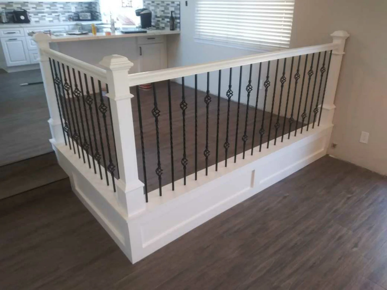 Completed residential railing and finish-carpentry improvement with white posts, black iron balusters, and updated flooring