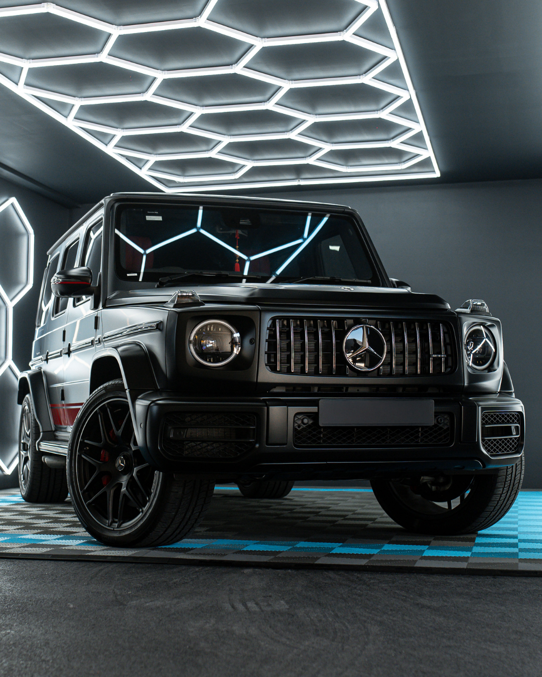 Black Mercedes-Benz G-Class SUV parked indoors with modern hexagon-shaped lighting on the ceiling and walls.