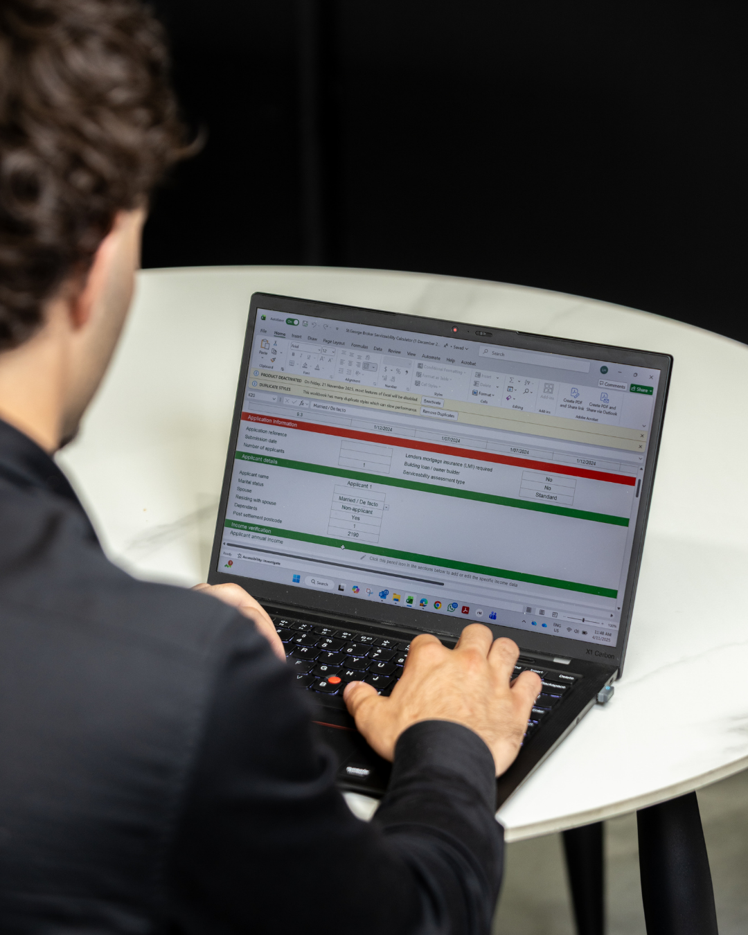 A person working on a laptop at a white table, viewing a spreadsheet with application and applicant details.