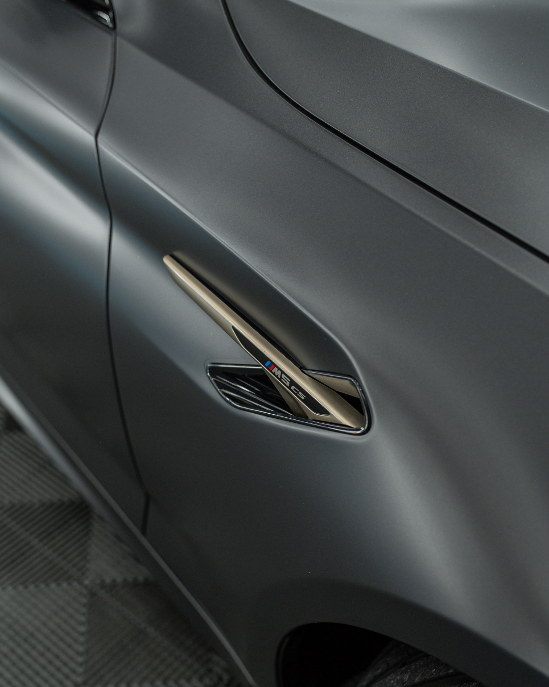 Close-up of a gray car with an M badge on the side vent, indicating a high-performance model.