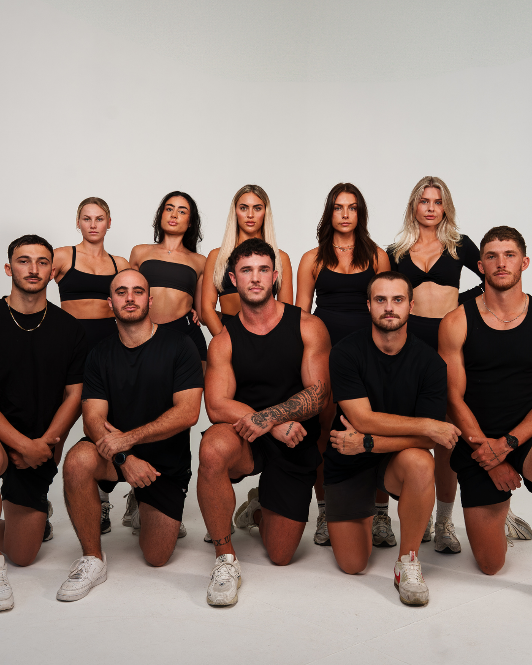 A group of ten young adults, six women and four men, posing shirtless and in athletic wear against a plain white background.