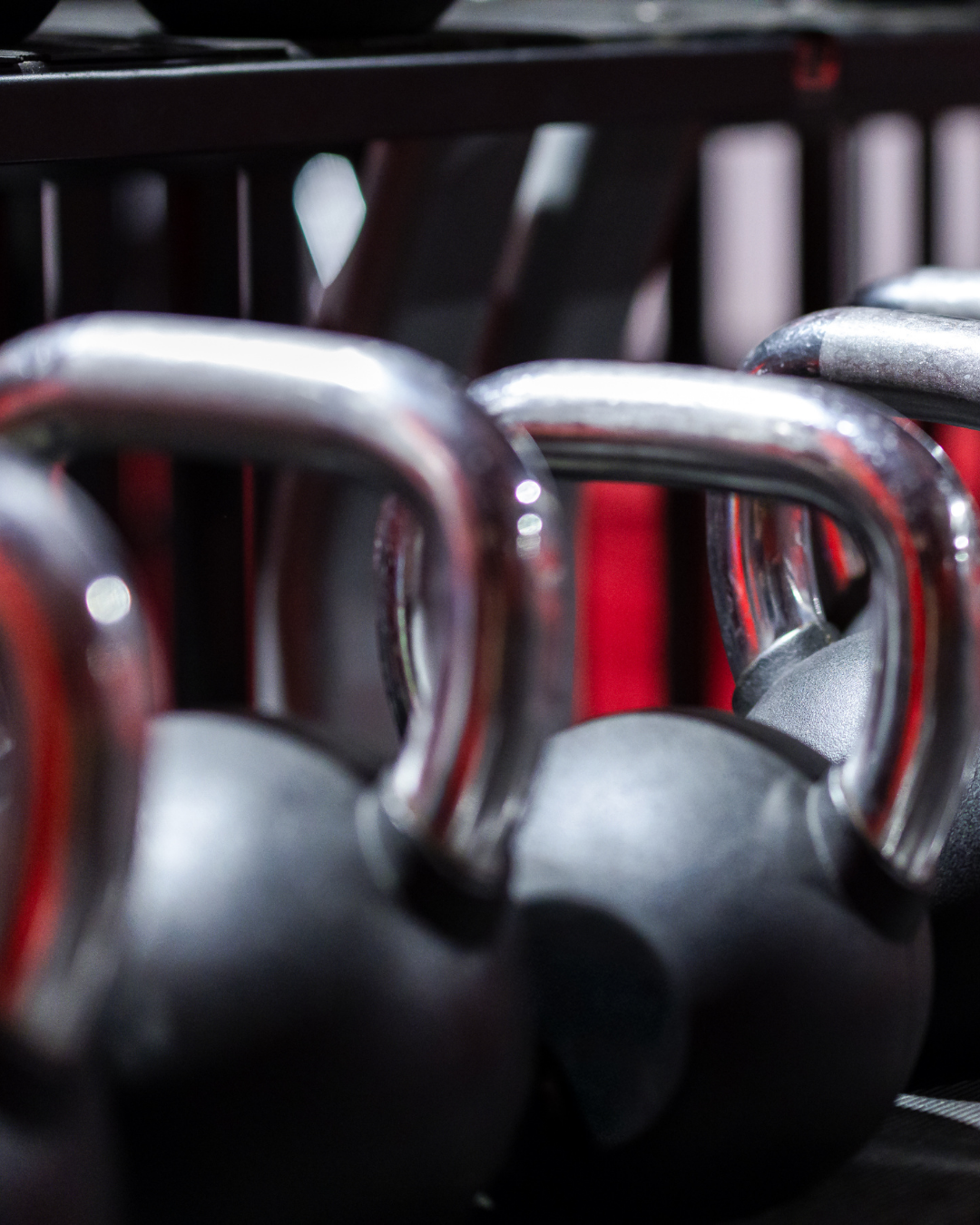 Close-up of black kettlebells with metal handles on a black workout mat.