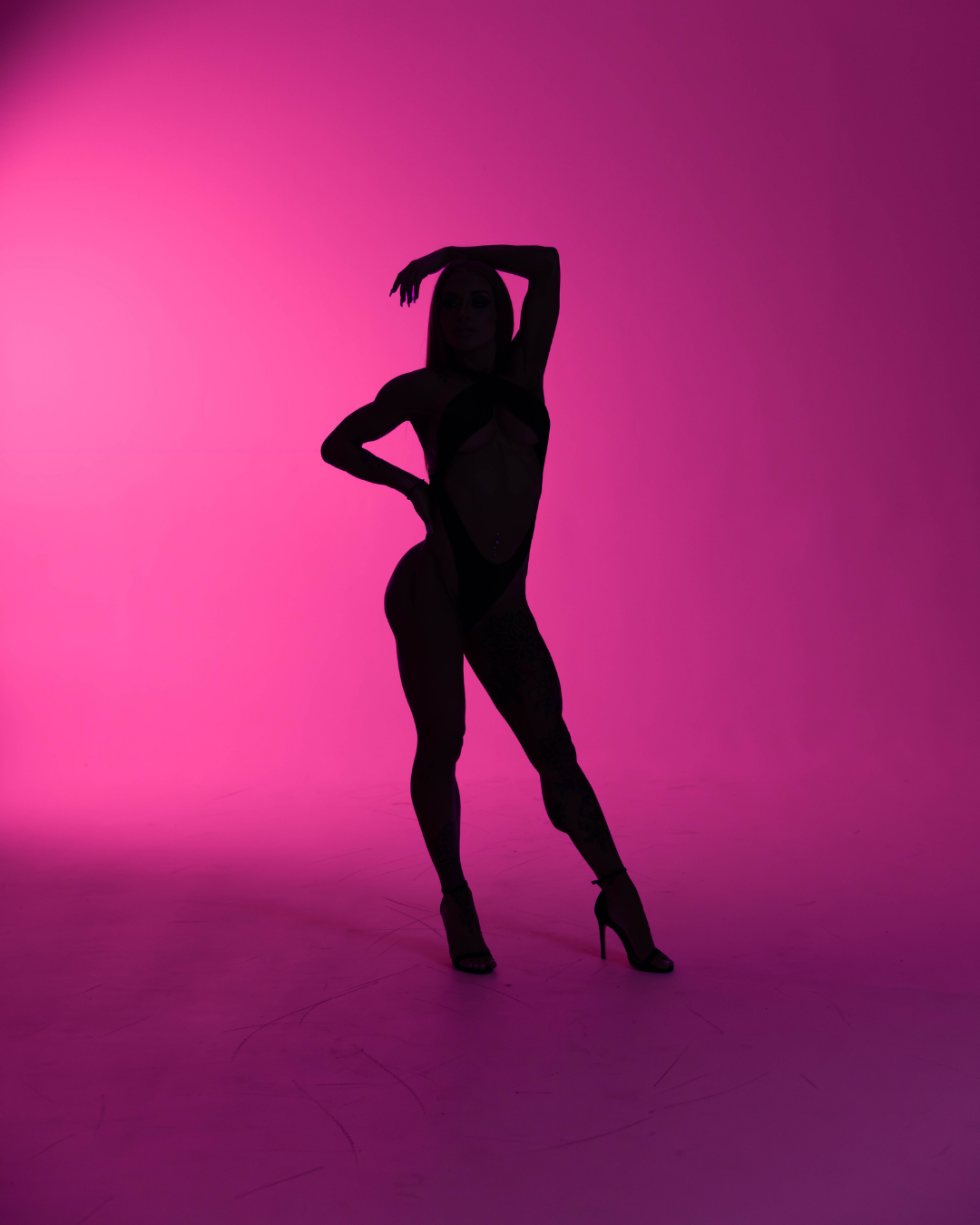 Silhouette of a woman in high heels standing and posing against a pink and purple gradient background.