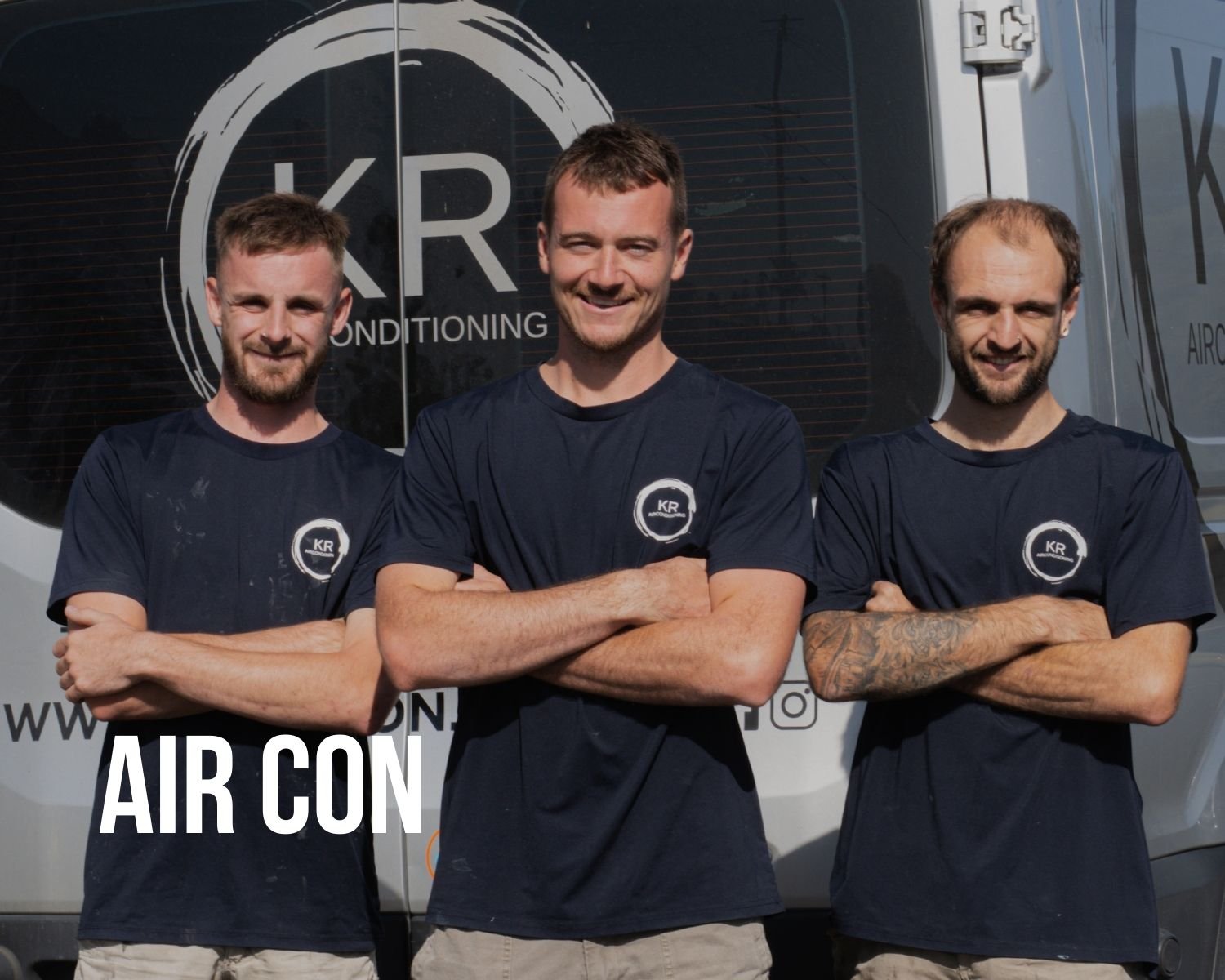 Three men standing with arms crossed in front of a truck with company logo, wearing navy blue t-shirts with company emblem, smiling.