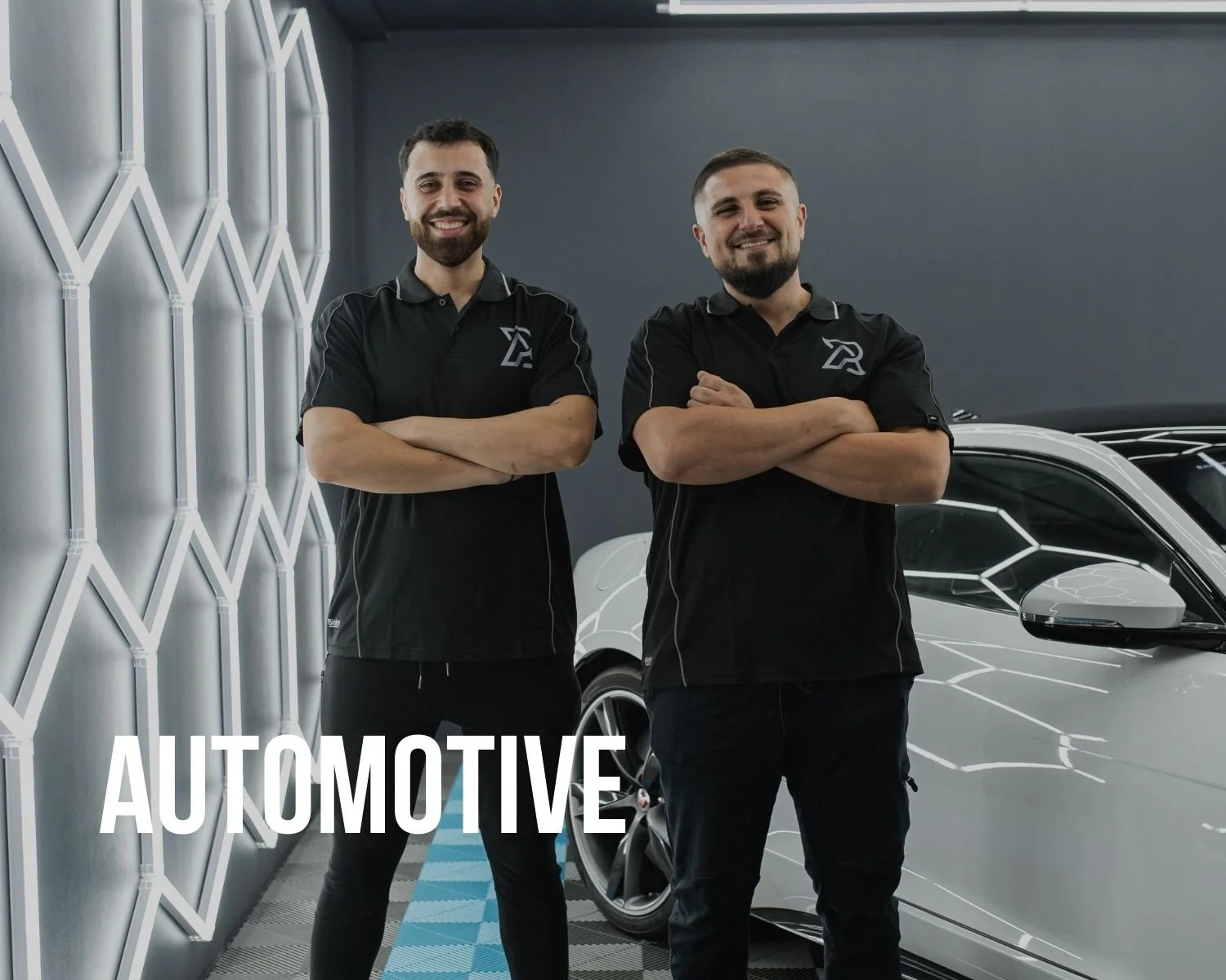 Two smiling men with crossed arms standing in an automotive showroom next to a white car with a modern interior design.