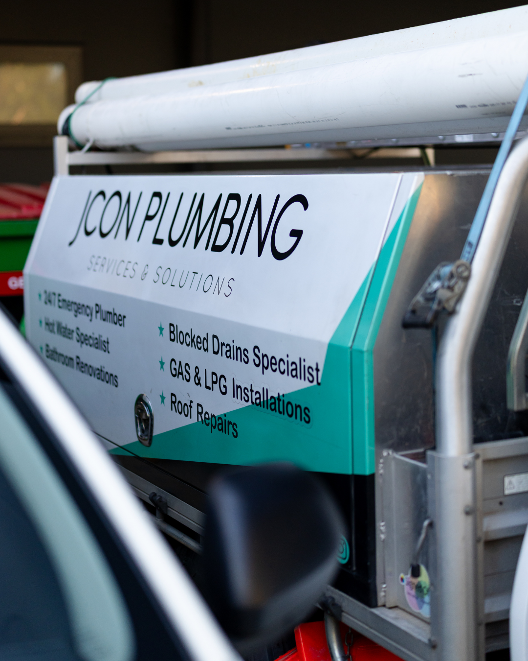 A sign on a service vehicle offering plumbing services, including emergency plumbing, drain blocking, gas and LPG installations, and roof repairs.