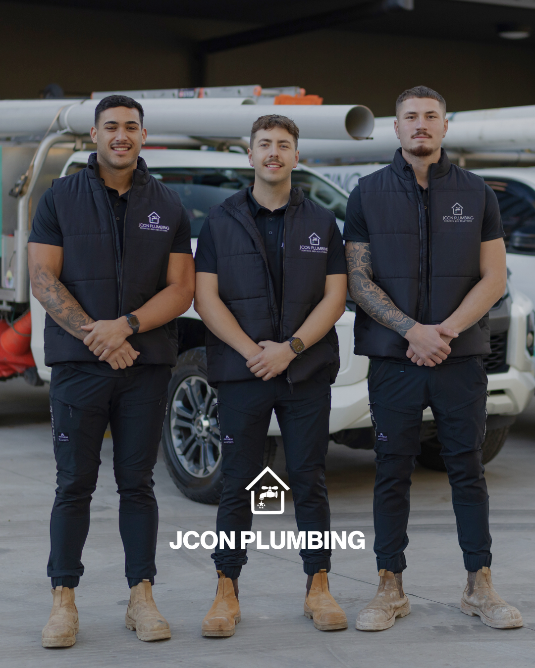 Three male plumbing technicians standing in front of a service van, wearing black vests with the 'JCON Plumbing' logo, and work boots. They are smiling and appear ready for work.