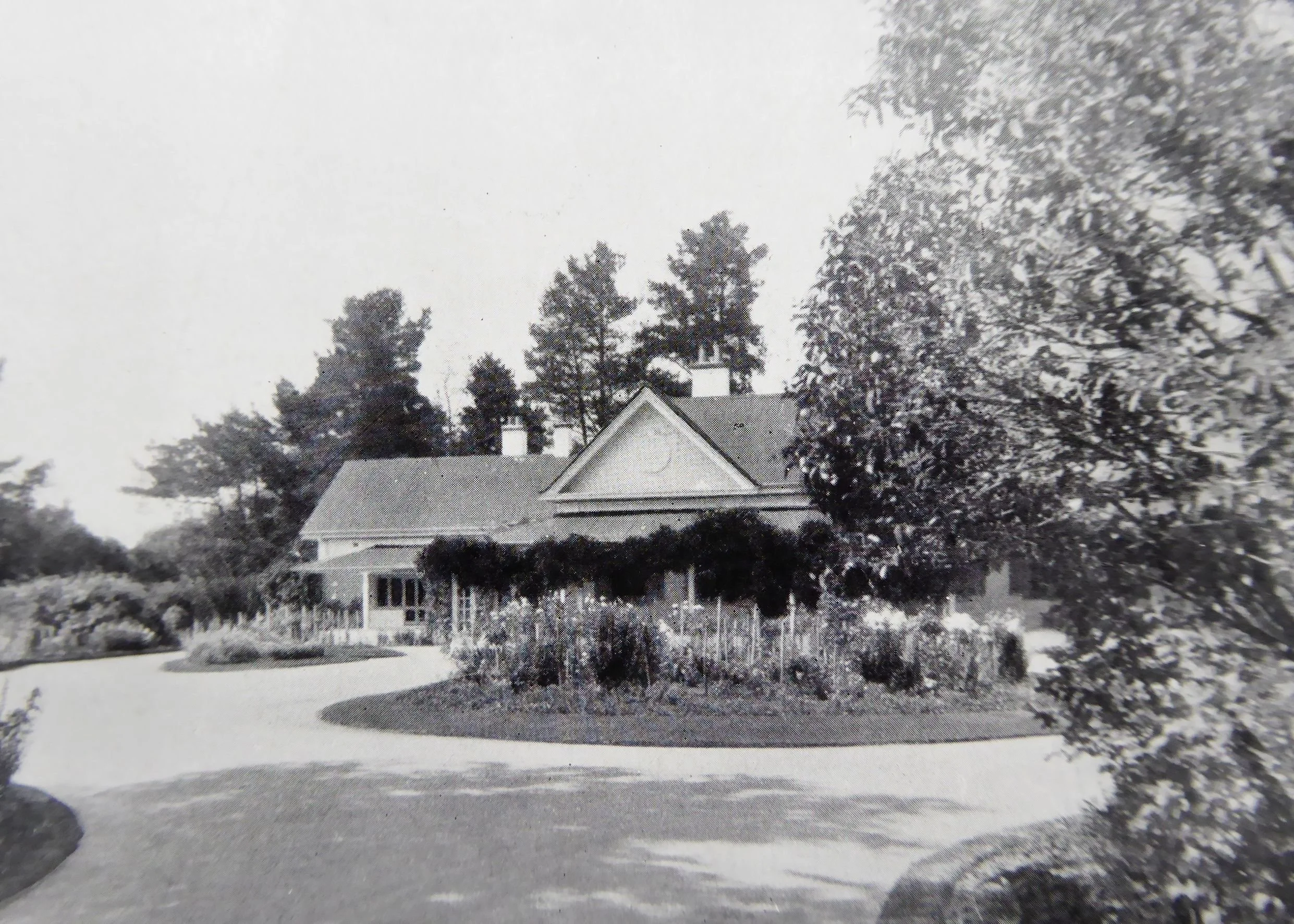 A historic black and white photograph of a large house with a gabled roof, surrounded by trees and a circular driveway.