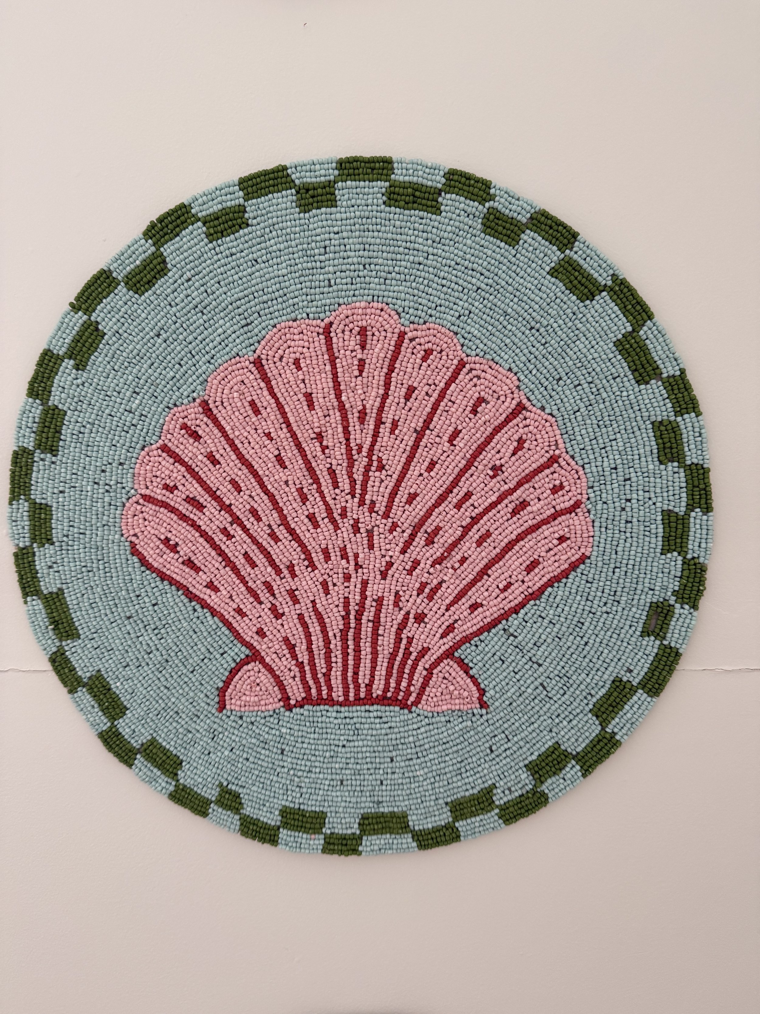 Beaded artwork featuring a pink seashell design on a round, woven background with a light blue and green border.