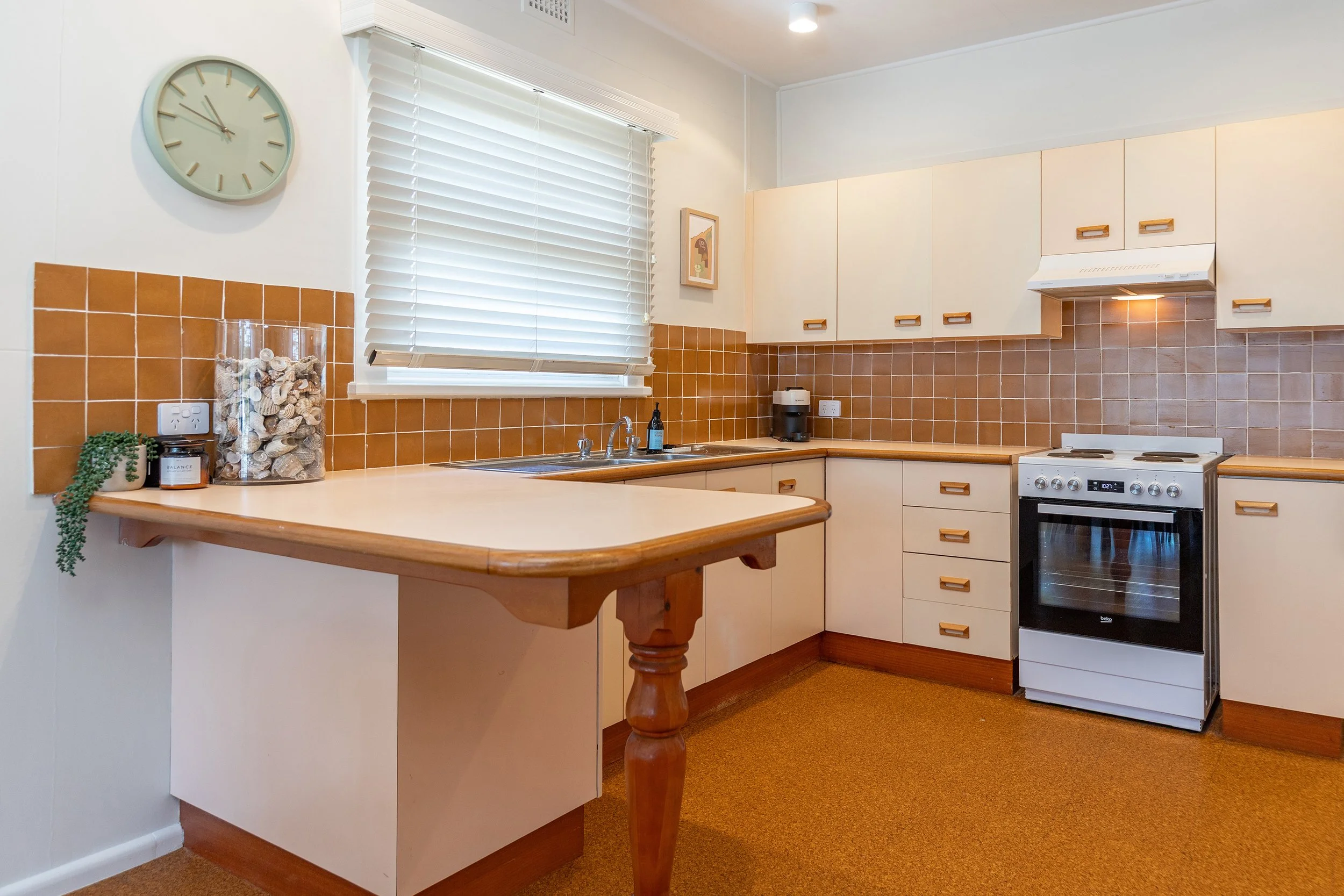 Kitchen with white cabinets, brown tiled backsplash, a window with white blinds, a gas stove, and a countertop with decorative items and appliances.