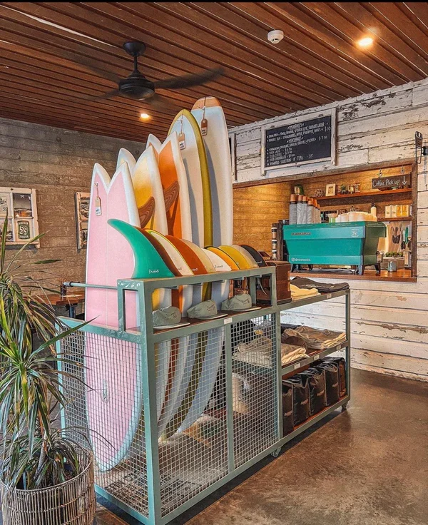 A display of colorful surfboards in a shop, with a surfboard rack and a coffee bar area in the background.