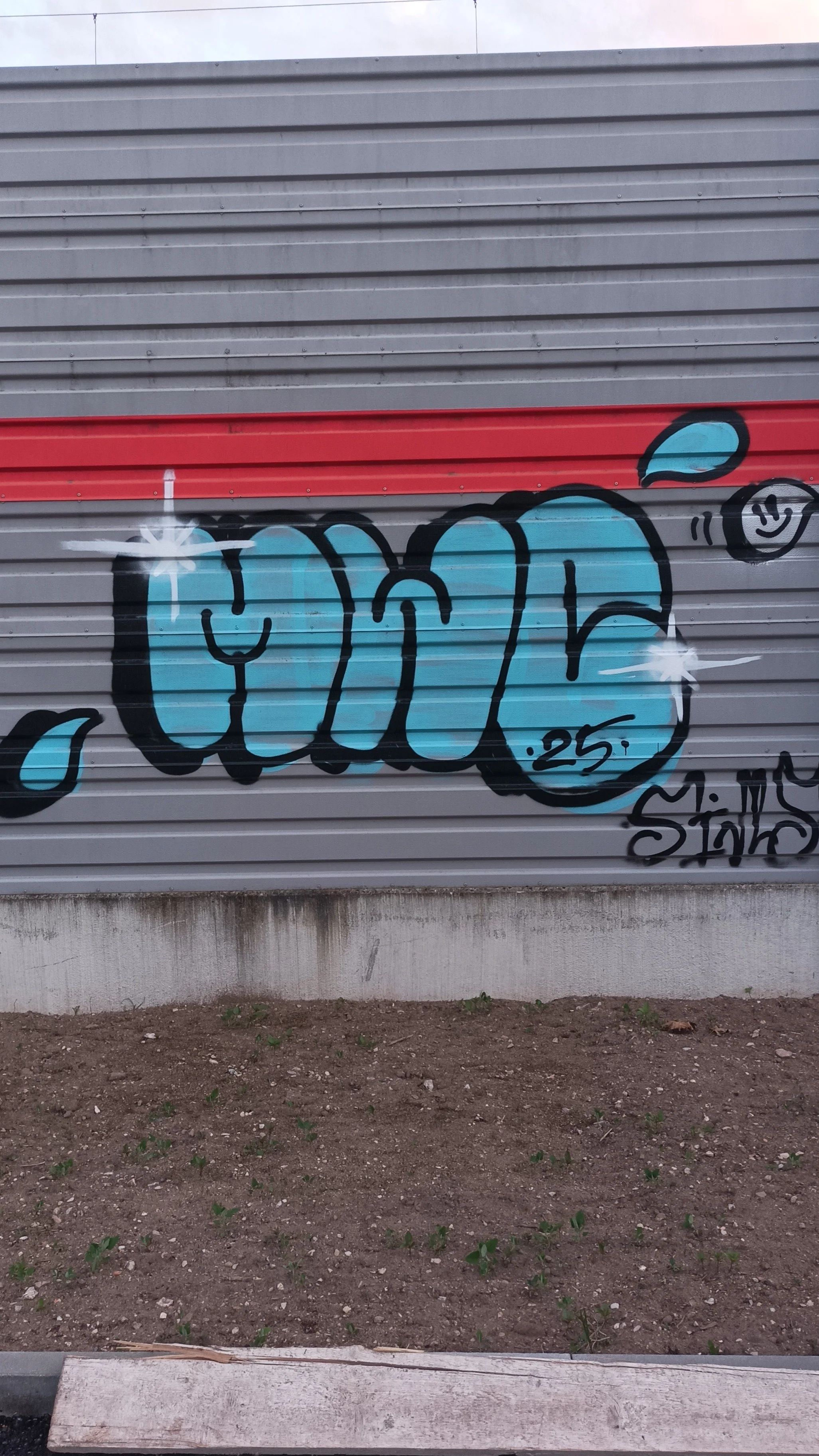 Graffiti auf einer Metallschiene, das Wort 'Cure' in blauer Schrift mit schwarzen Umrissen, begleitet von einem lachenden Gesicht und Wassertröpfchen, mit der Nummer 25 und dem Namen 'M. Sinb' darunter.
