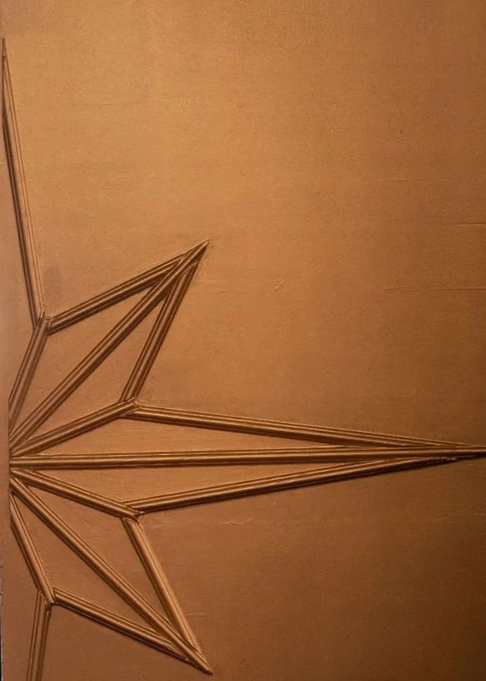A star-shaped decoration made of thin metallic rods on a beige wall.