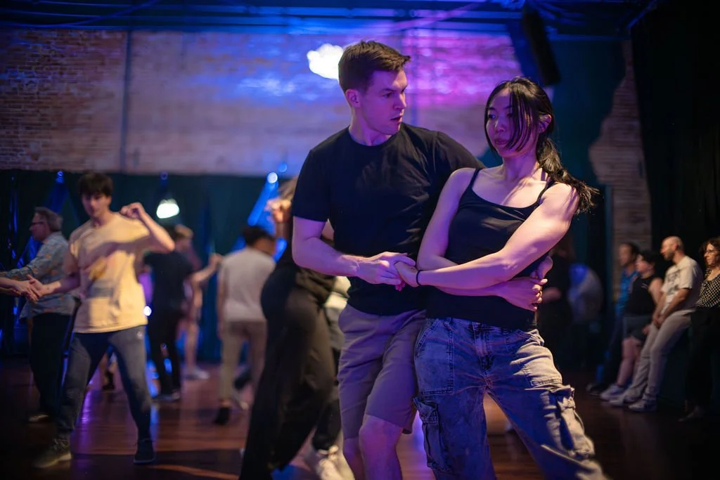 Couple dancing closely in a dimly lit dance hall with other dancers in the background.