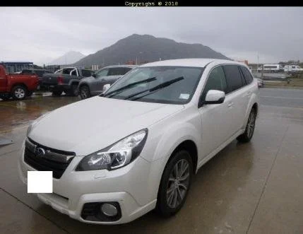 White Subaru Outback parked on wet pavement with mountains in the background.