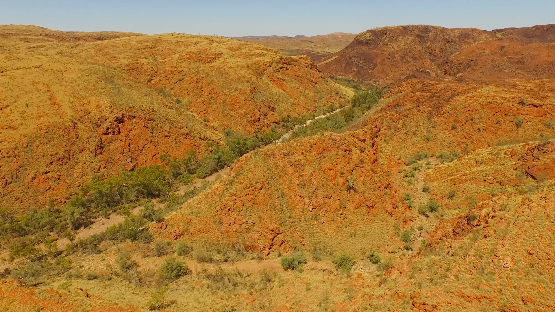 Aerial view of red and orange rugged desert hills with sparse green vegetation and dirt paths.