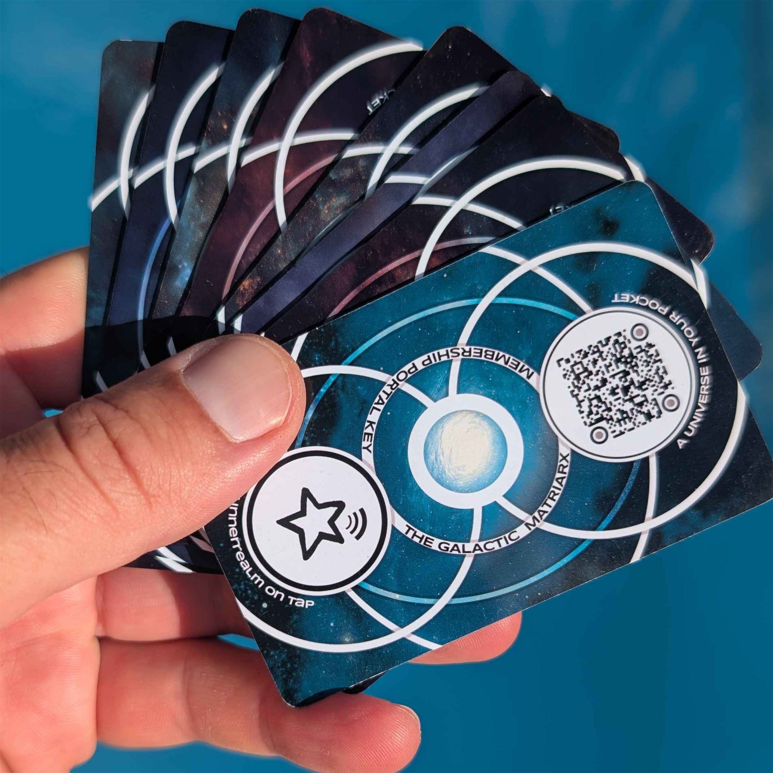 A hand holding a set of playing cards with space-themed designs, featuring an image of the galaxy and a QR code.